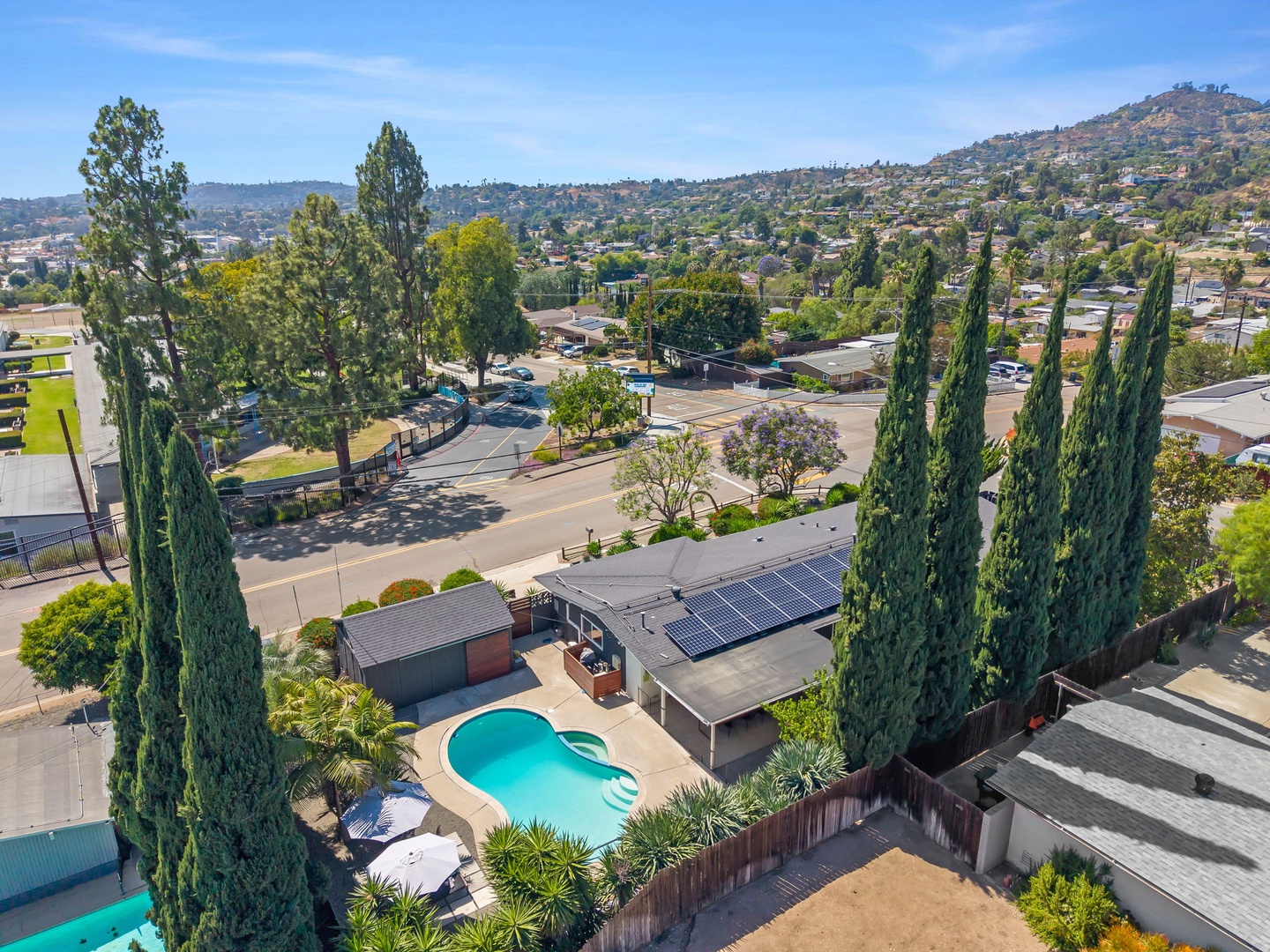 Aerial view of the property nestled in a hillside neighborhood, featuring a resort-style backyard and sparkling pool