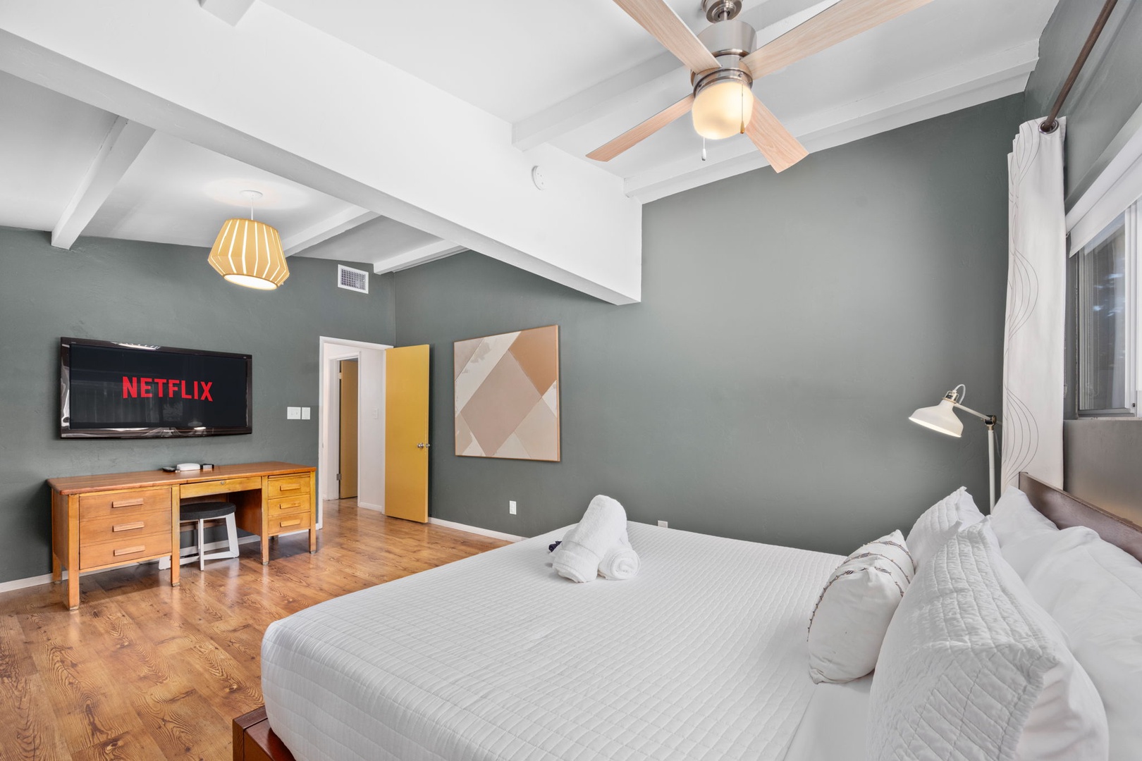Sink into crisp white linens and wake to soft natural light in this serene primary bedroom. Mid-century wood furnishings and curated art warm calming sage walls, creating your peaceful retreat. Private ensuite bathroom and walk in closet.