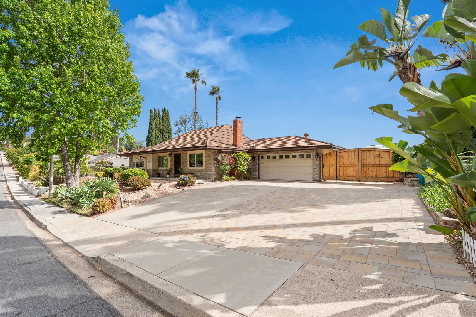 Single-story home featuring stone and brick exterior with tile roof, surrounded by mature landscaping and palm trees in sunny residential neighborhood.