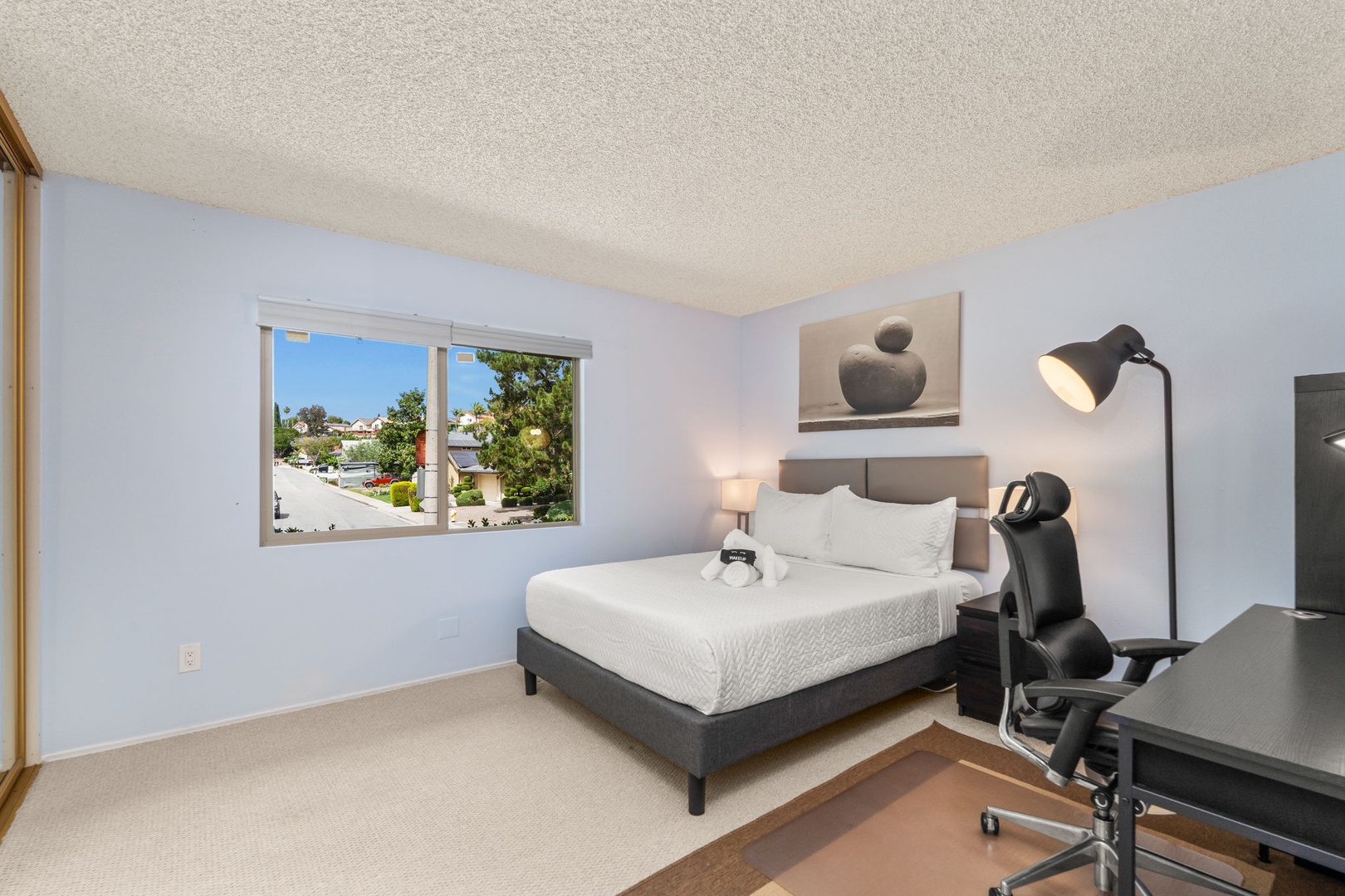 Your comfortable bedroom features a queen bed, modern desk workspace, and bright window with peaceful neighborhood views for a productive stay.