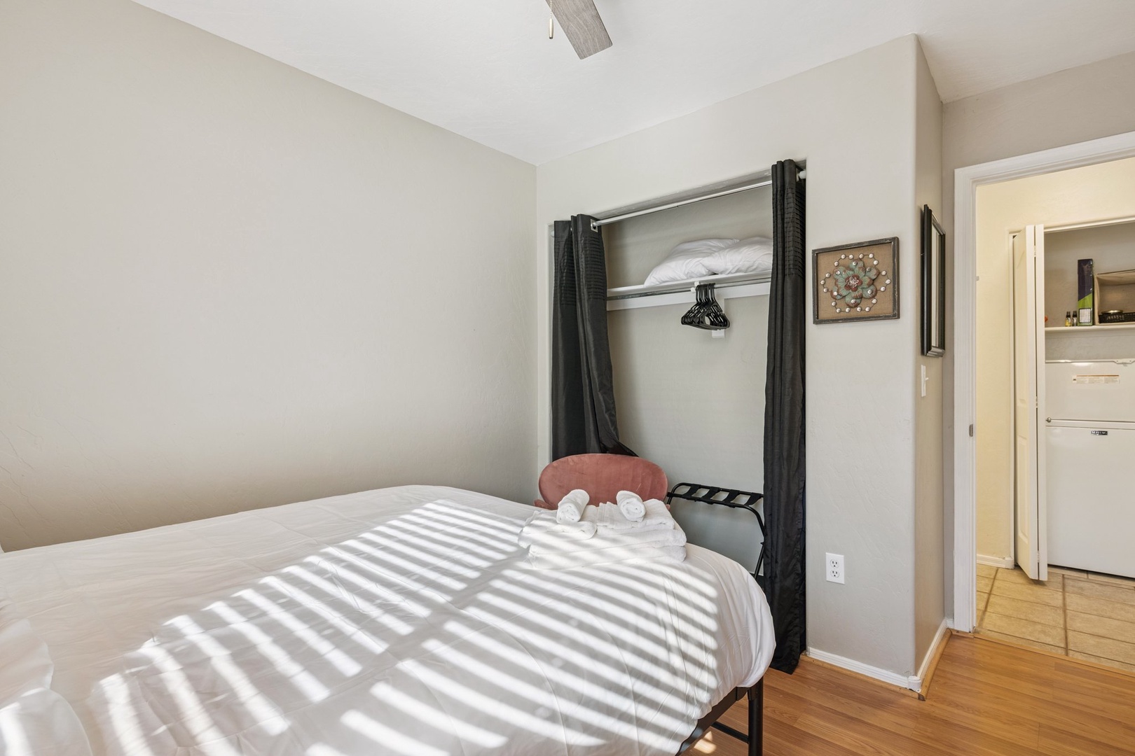 Your cozy bedroom features crisp linens and thoughtful storage, with warm sunlight streaming through to create peaceful shadows across the space.