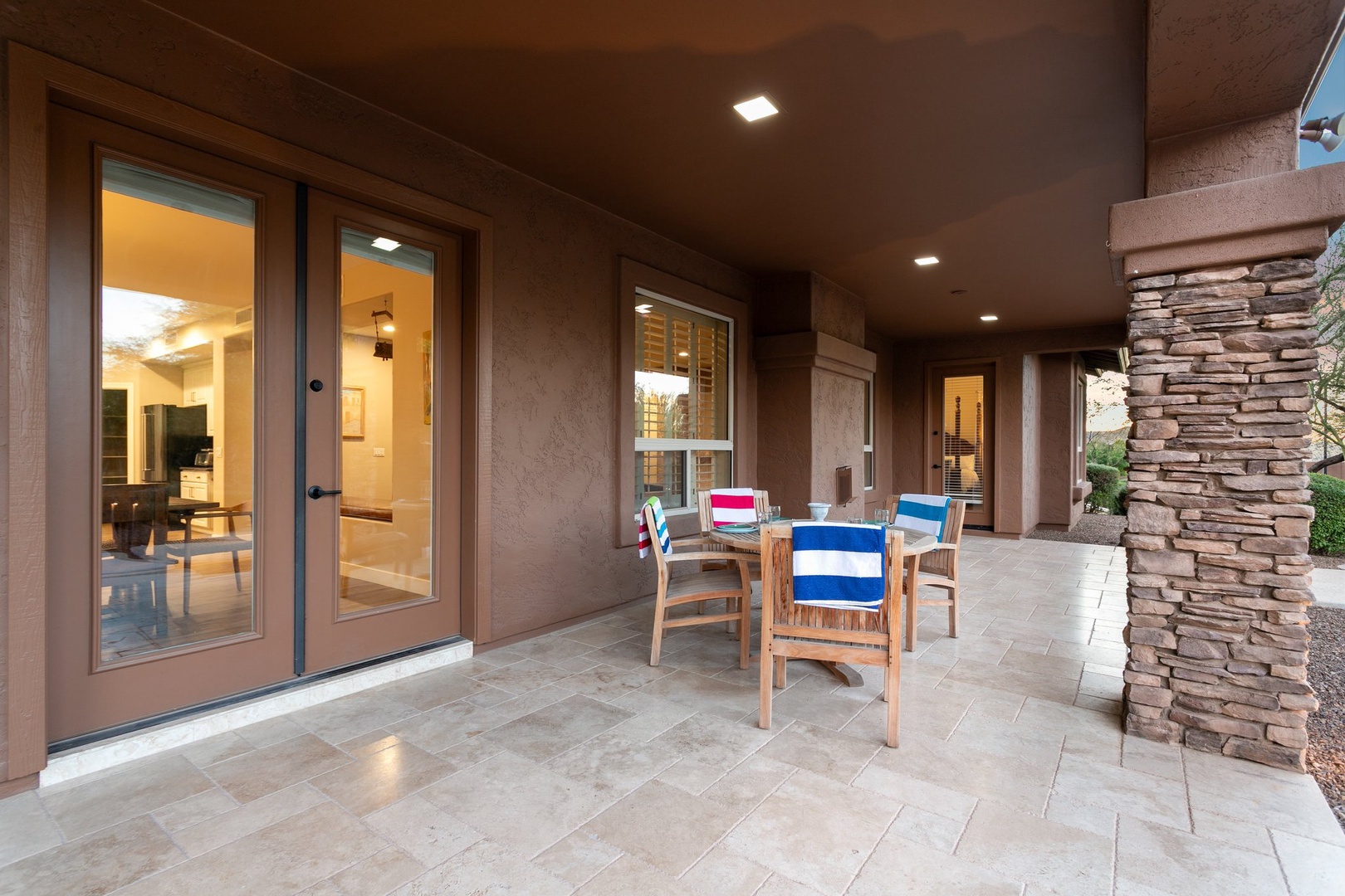 Your covered patio beckons with comfortable seating and stone accents, perfect for morning coffee or evening relaxation while staying connected to the bright, welcoming interior.