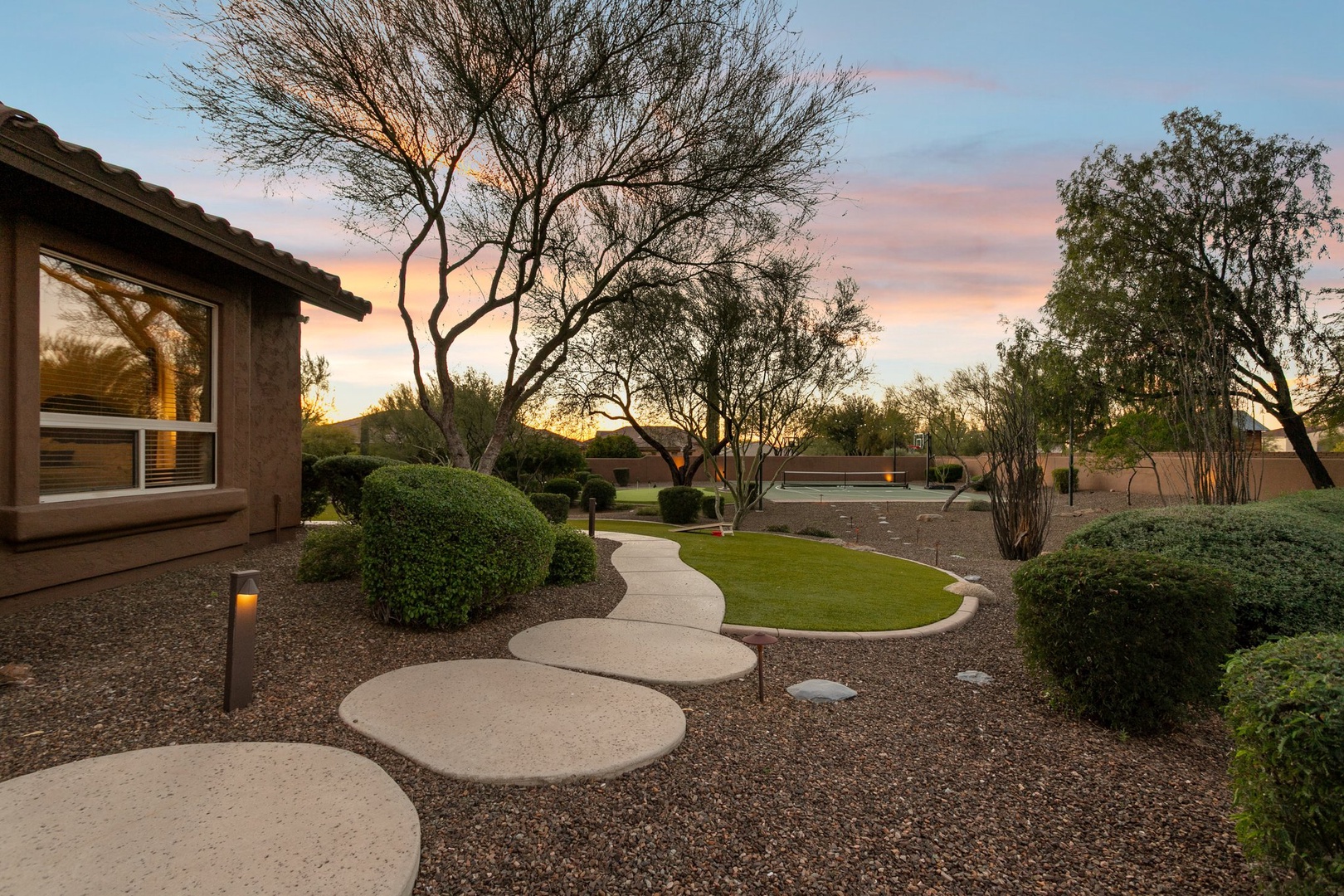 Beautiful desert landscape surrounds the property with mature trees and thoughtfully designed pathways leading through manicured grounds at sunset.