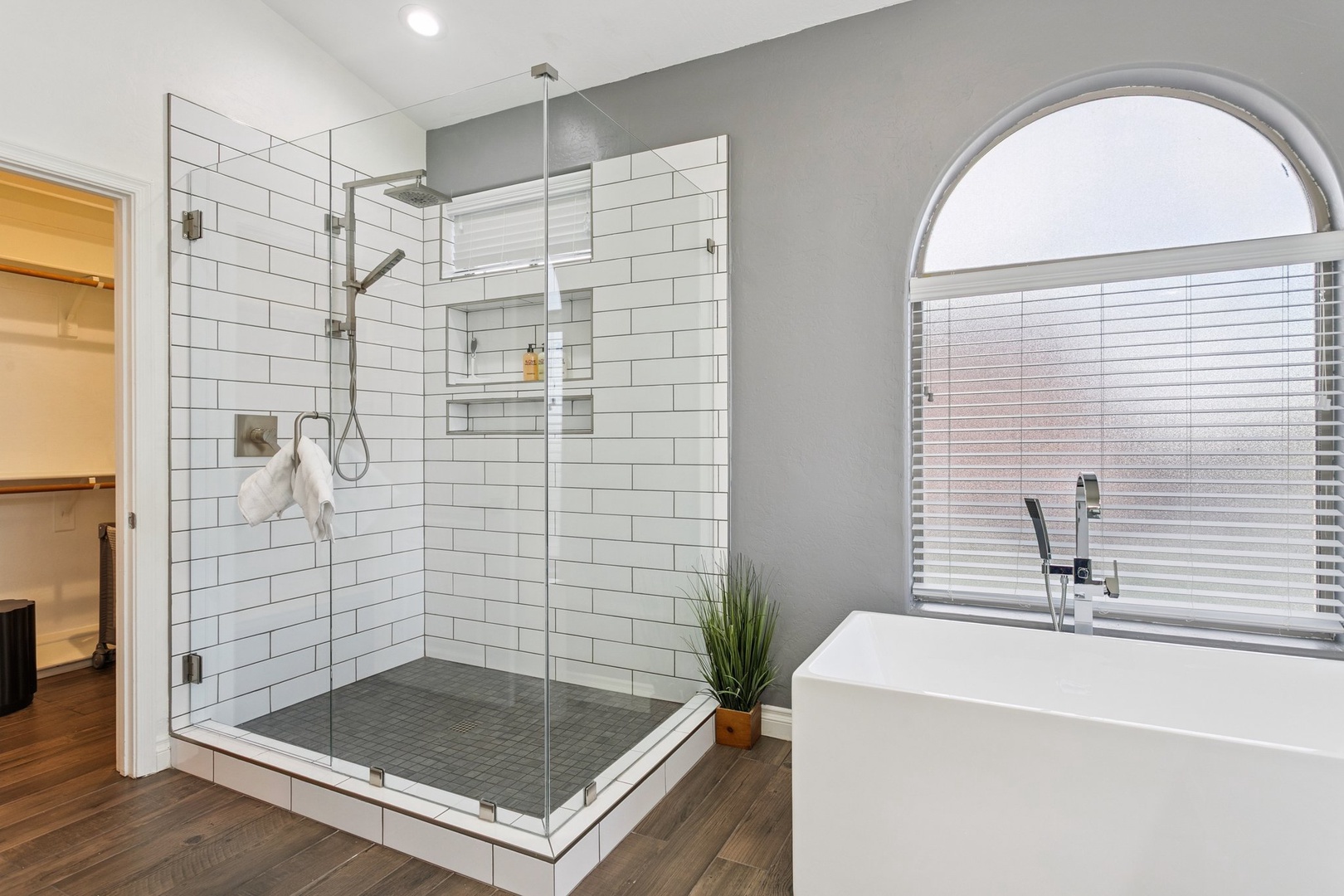 Unwind in your spa-like bathroom featuring a spacious glass shower and soaking tub beneath an elegant arched window.