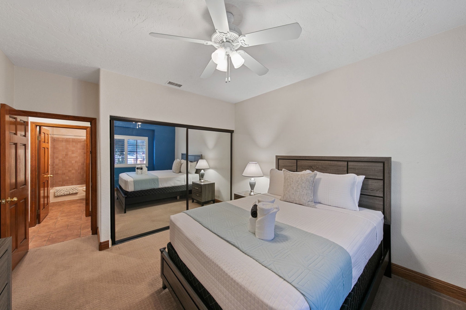 Relax in this queen bed with plush bedding, ceiling fan, and mirrored closets reflecting natural light throughout the space.