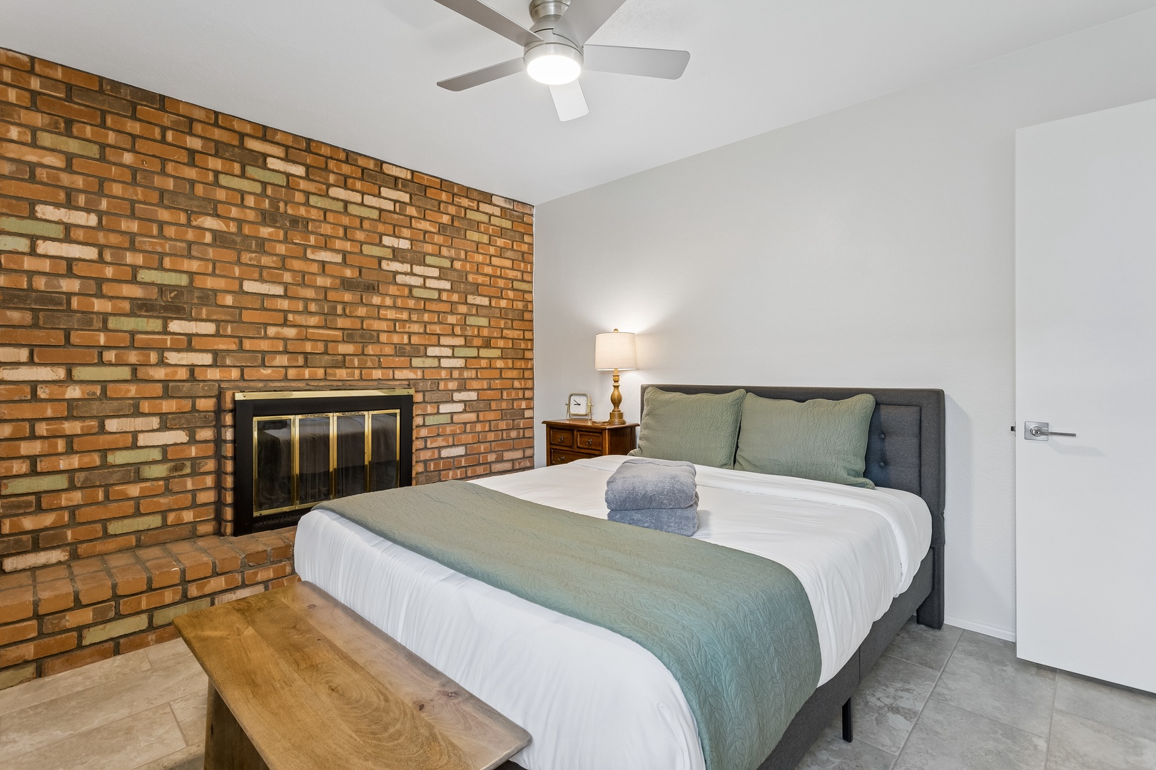 Unwind in your cozy bedroom, where warm brick meets modern comfort. Sink into plush bedding beside a glowing fireplace, with a ceiling fan keeping the air just right for restful nights.