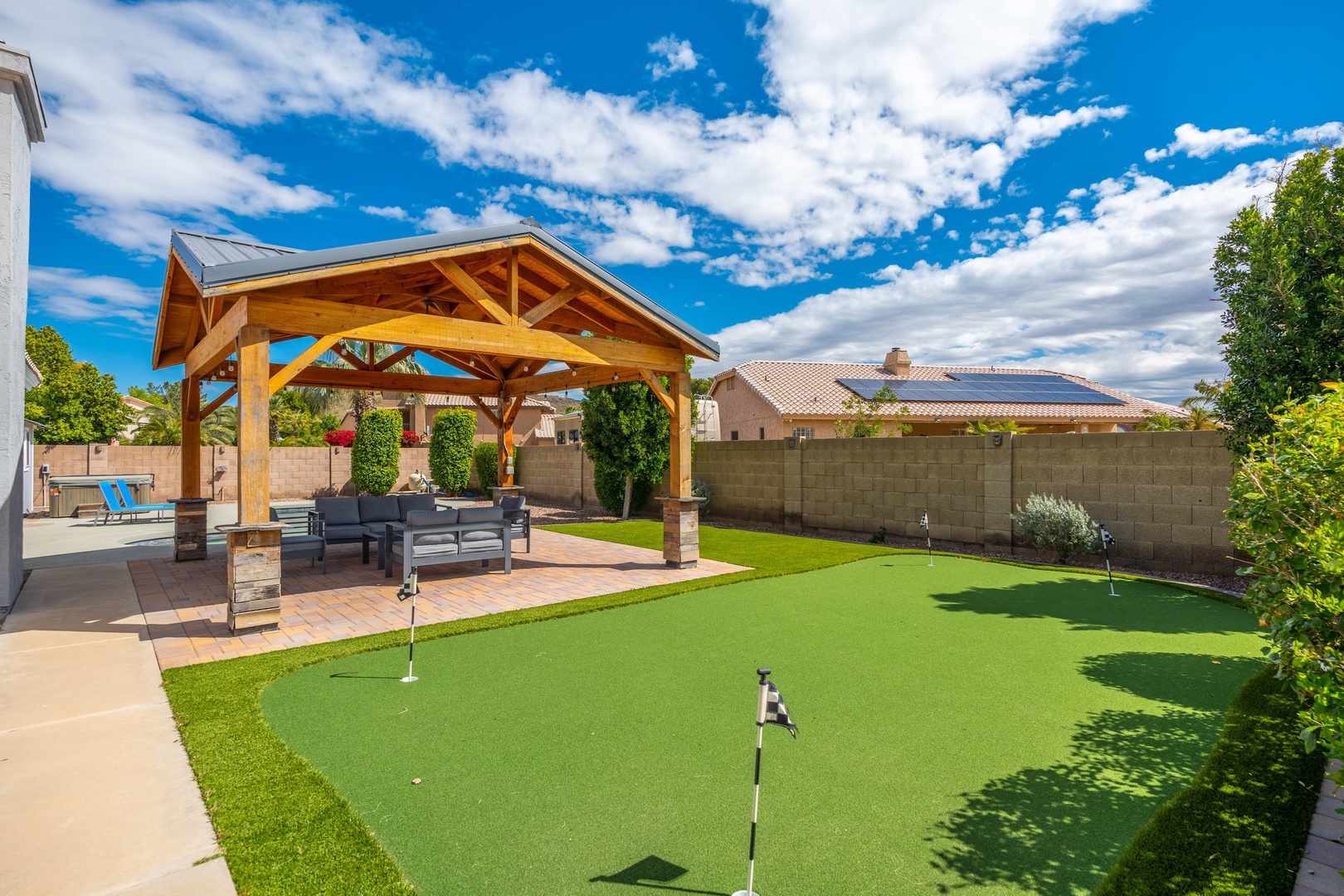 A private backyard putting green awaits alongside a covered patio with comfortable seating, perfect for outdoor practice and relaxation under open skies.