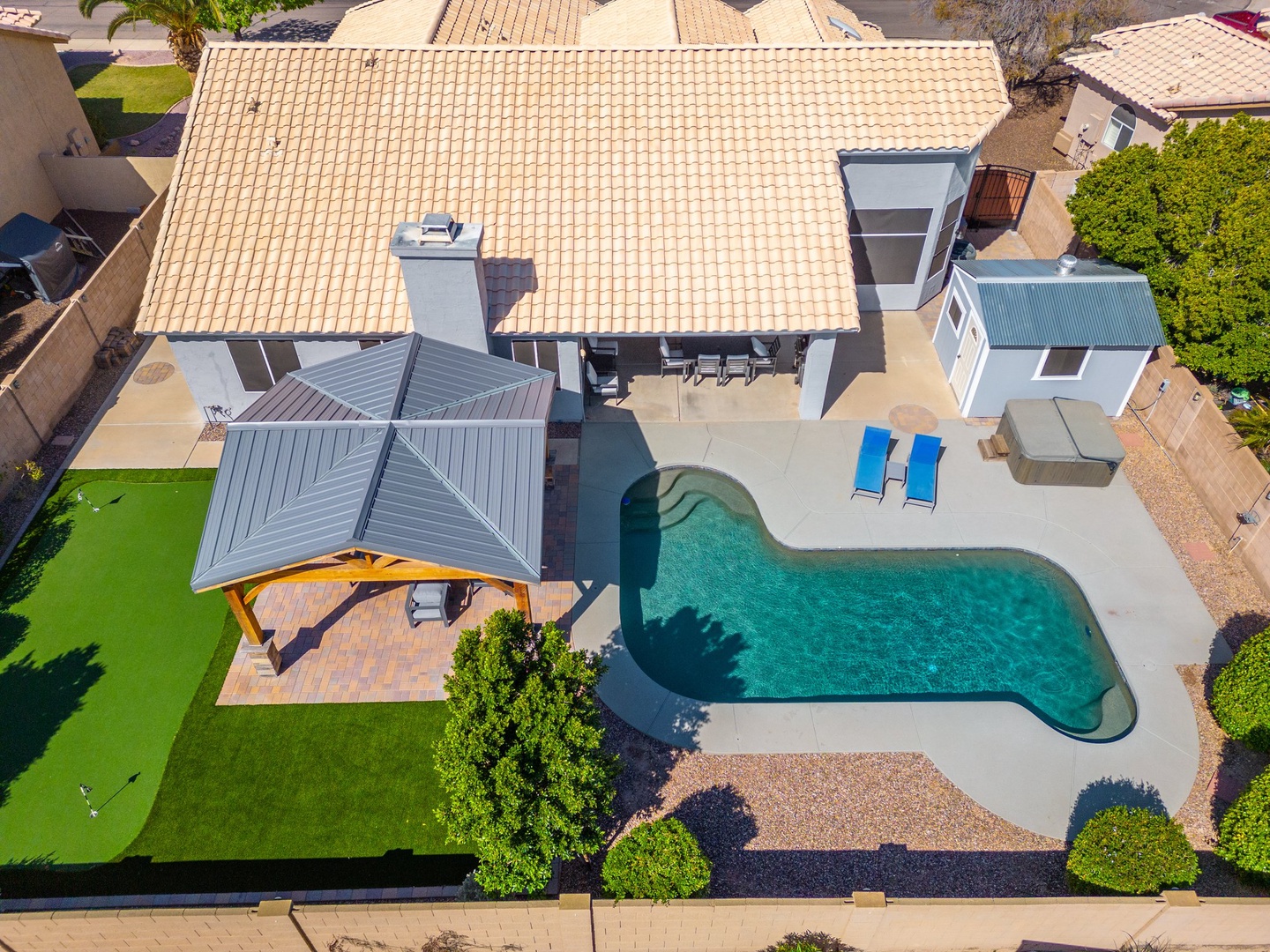 Aerial view of the property showcasing a private pool, covered patio with dining area, and well-maintained grounds surrounded by residential neighbors.