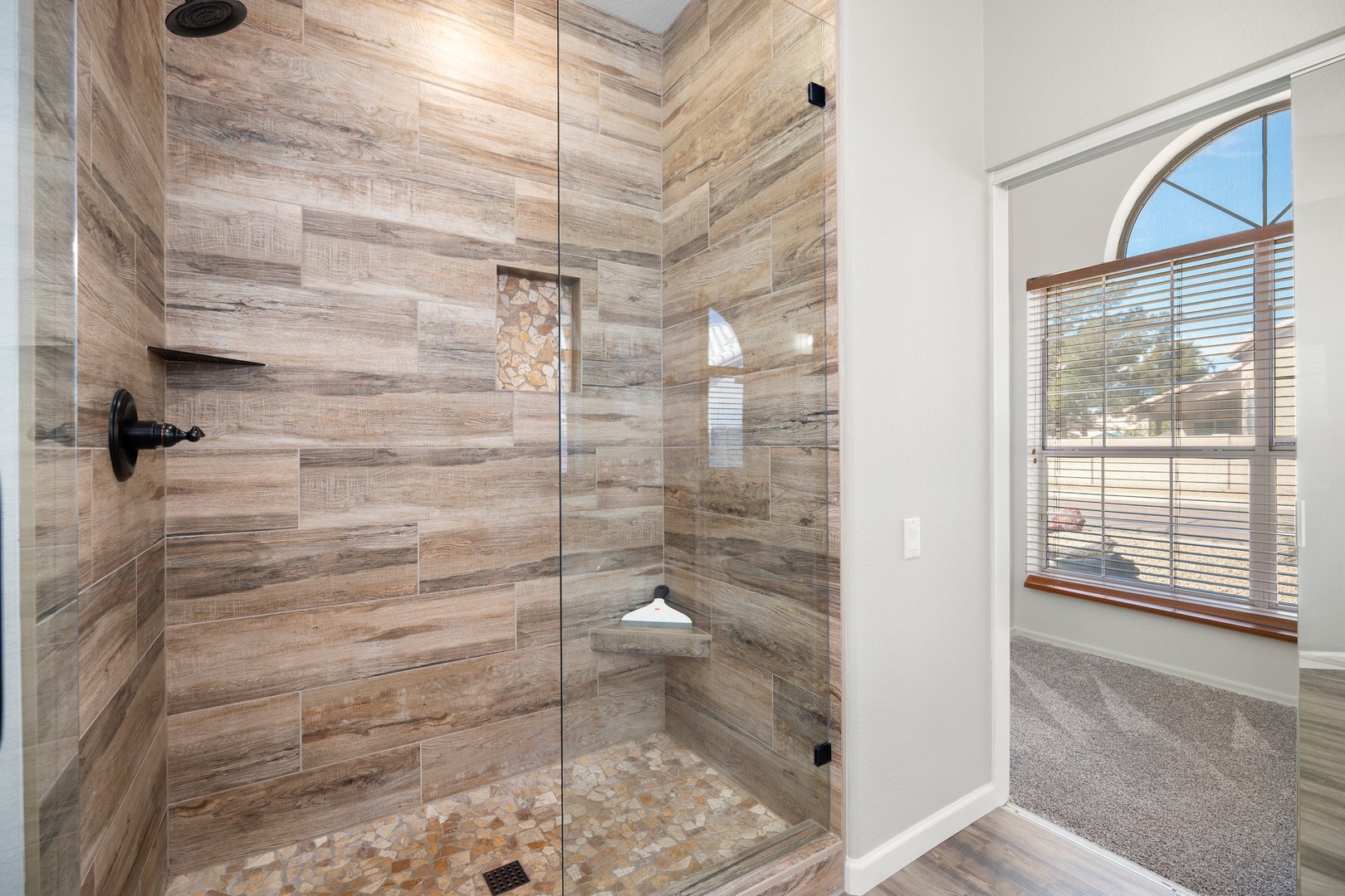 Primary suite bathroom is a spa-like retreat with stunning wood-look tile enveloping the walk-in shower.