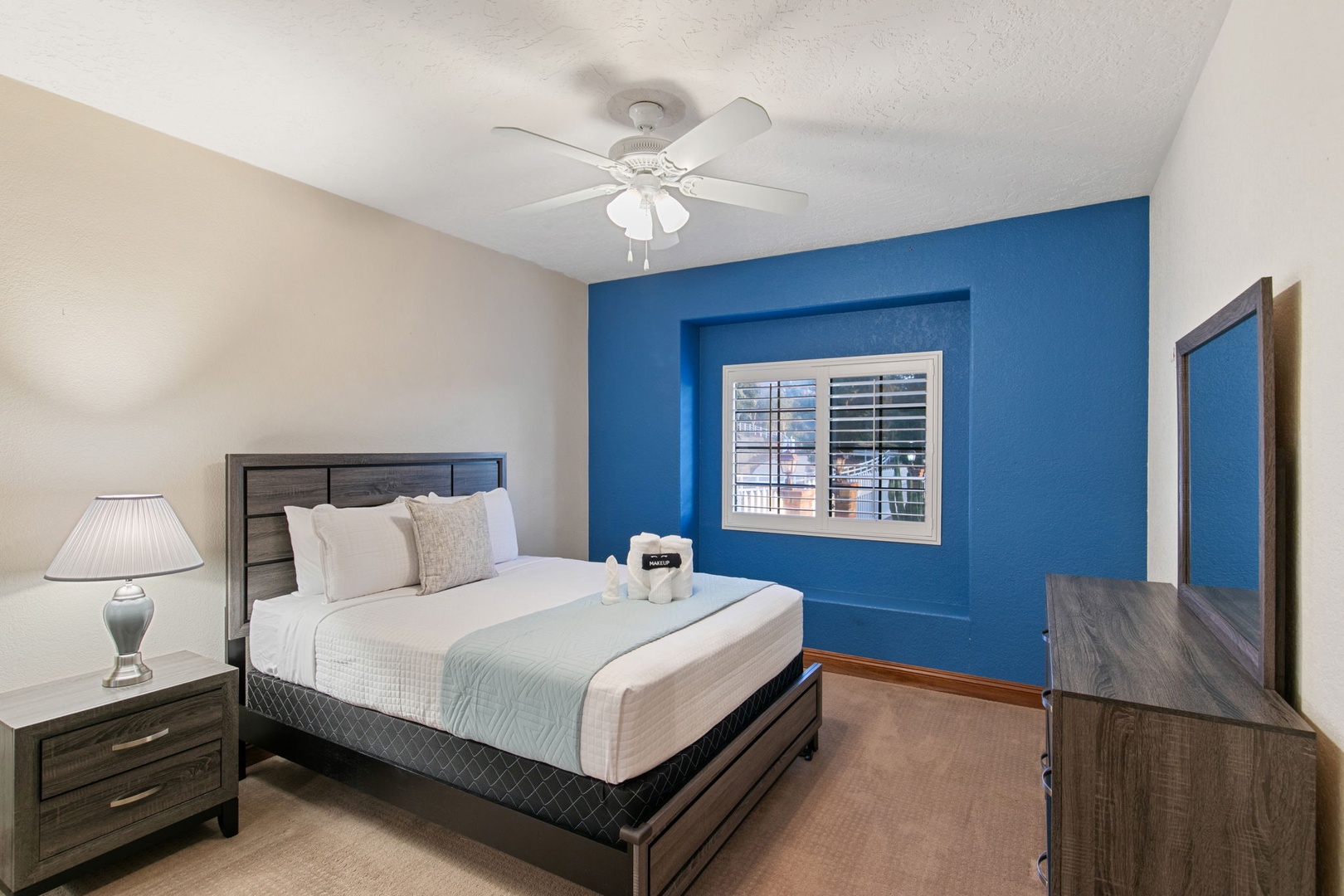 Unwind in your serene bedroom featuring a cozy queen bed, vibrant blue accent wall, and ceiling fan for perfect comfort.