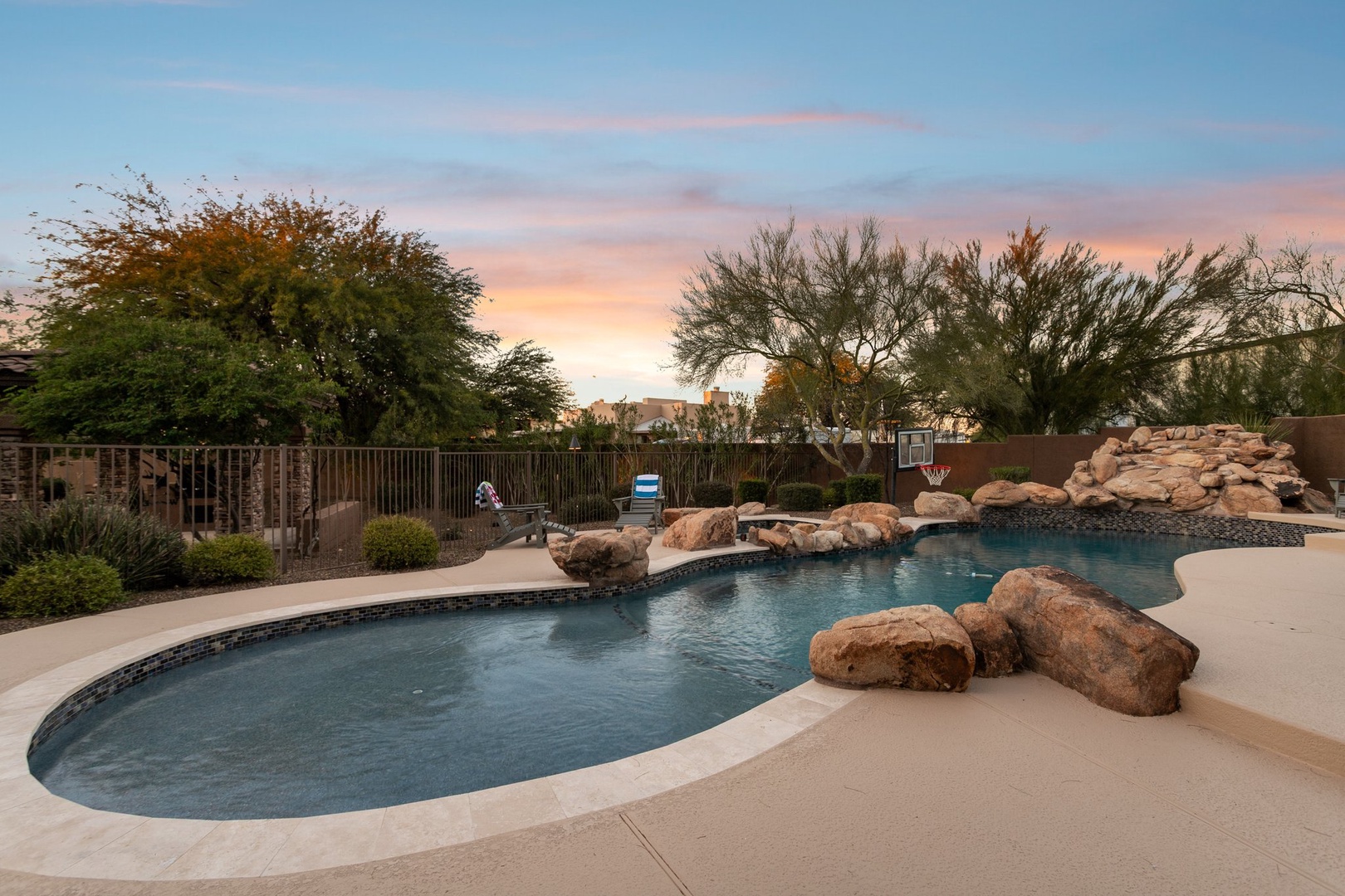 Stunning resort-style pool with natural rock features and desert landscaping under a painted sunset sky.