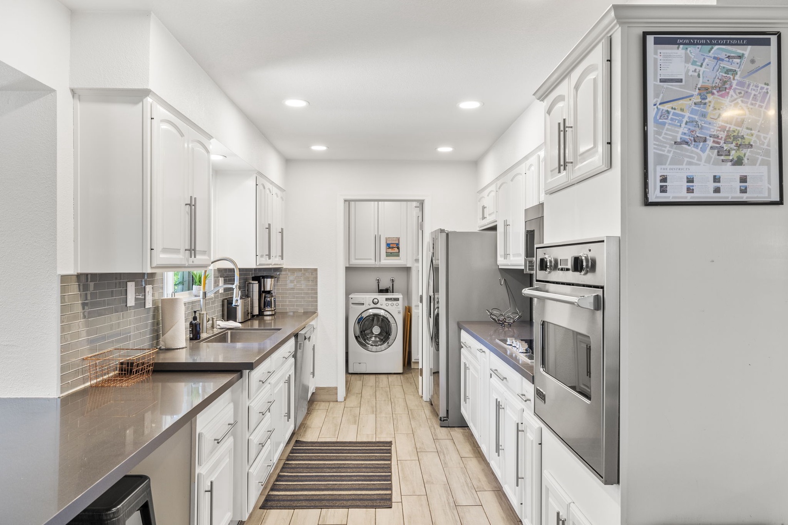 Kitchen has modern stainless steel appliances including: dishwasher, fridge, stove top, coffee maker, pots and pans, and utensils.