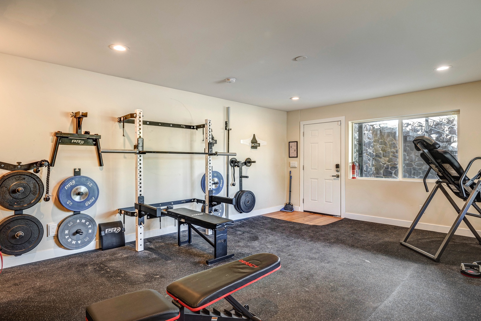 Fitness room with bench, squat rack, dumbbells, flat bench, & kettle bells.