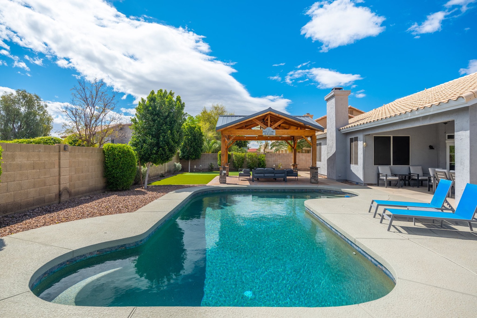 The private oasis awaits with a sparkling pool, covered pavilion for alfresco dining, and expansive patio surrounded by lush greenery—perfect for sunny desert relaxation.
