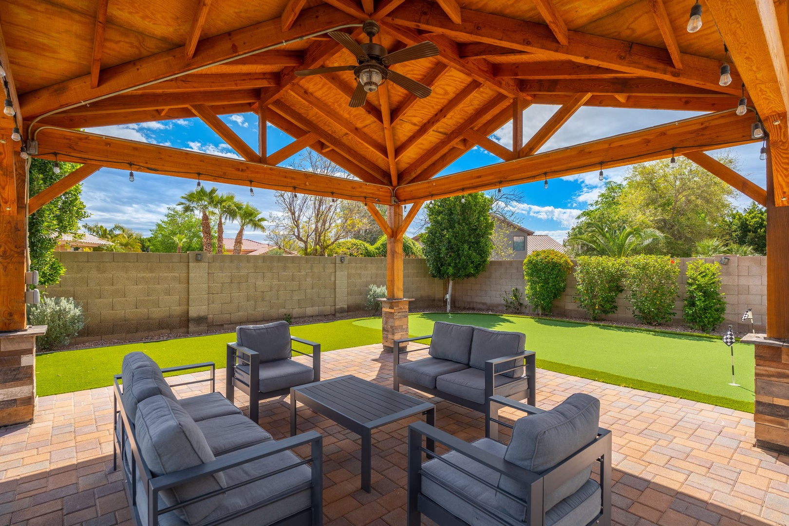 Picture yourself relaxing under this stunning wood-beamed pavilion, where comfortable seating invites you to unwind overlooking your private, lush green lawn surrounded by mature palms and hedges.