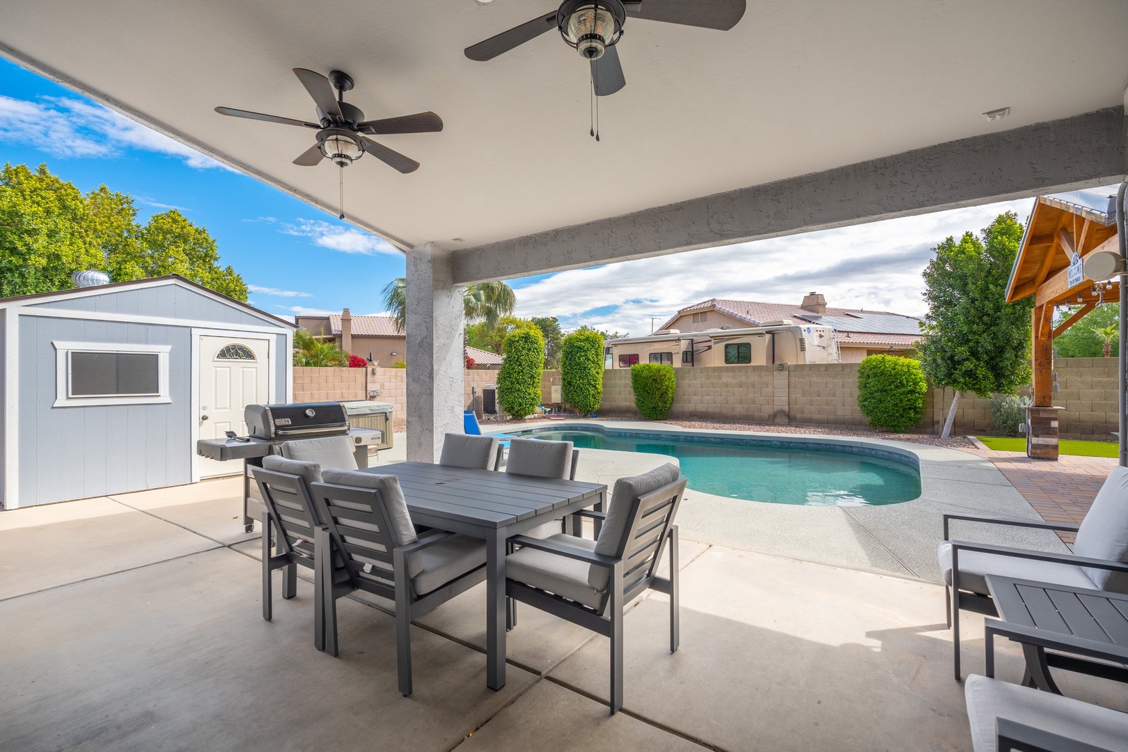 A private backyard oasis featuring a sparkling pool and covered patio with ceiling fans, perfect for outdoor dining and sunny Arizona days.