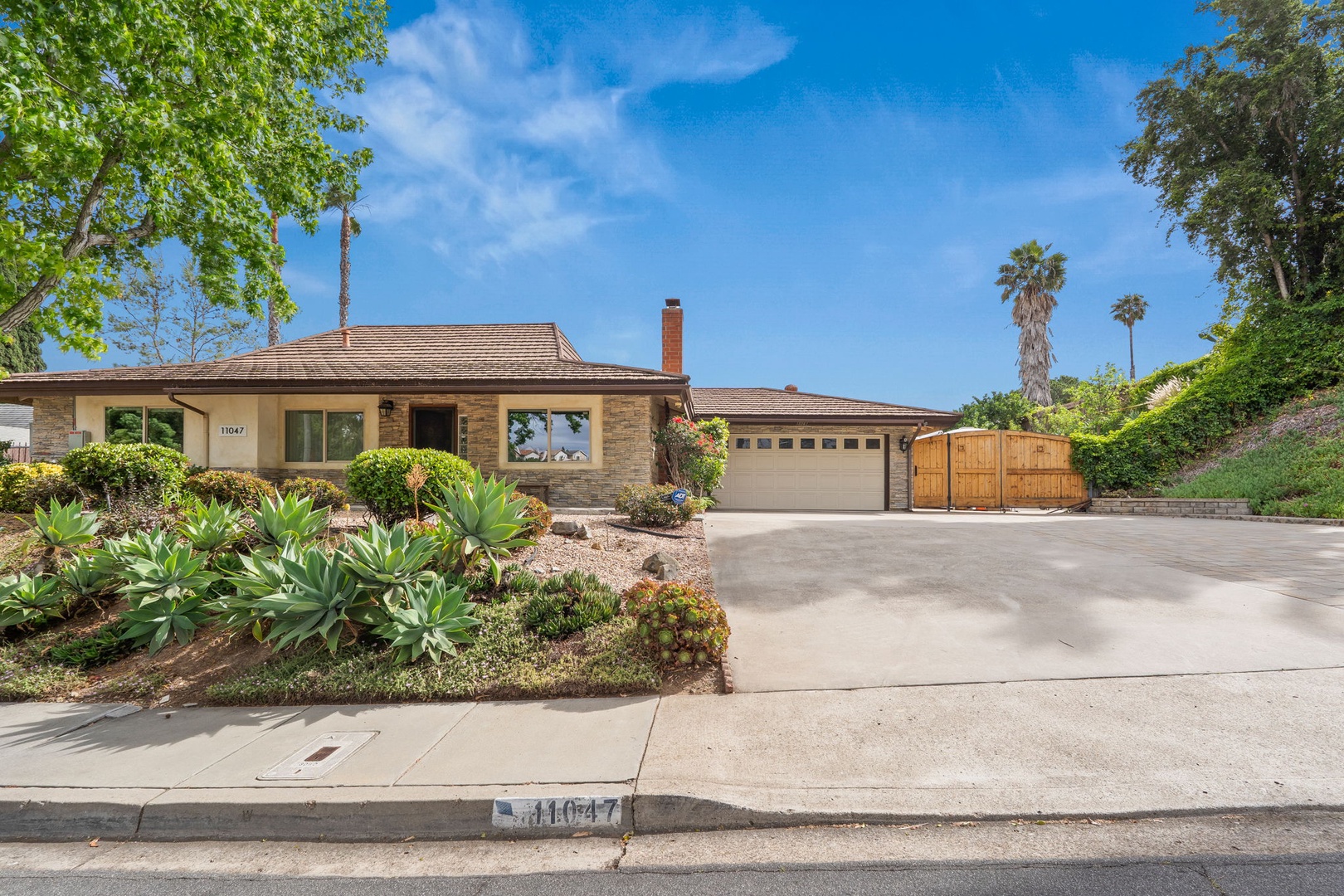 Charming single-story home with beautifully landscaped front yard featuring desert plants and mature trees in a peaceful residential setting.