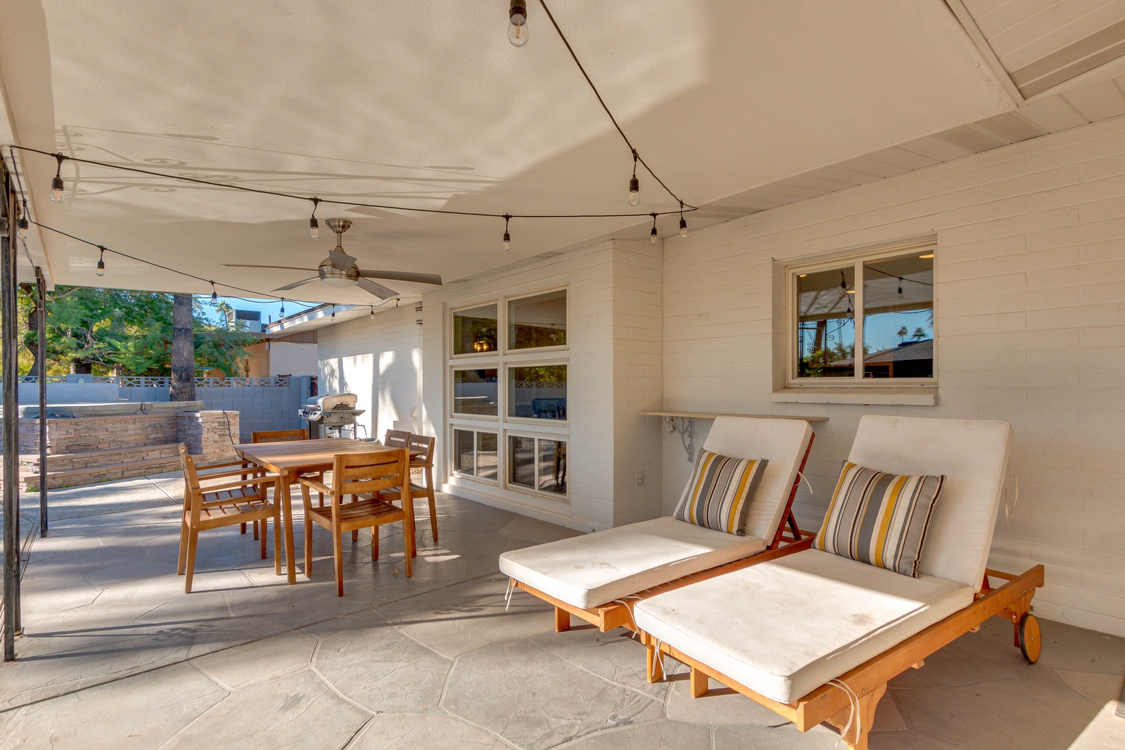 Spacious covered patio with loungers and table. Pool and hot tub in the back.