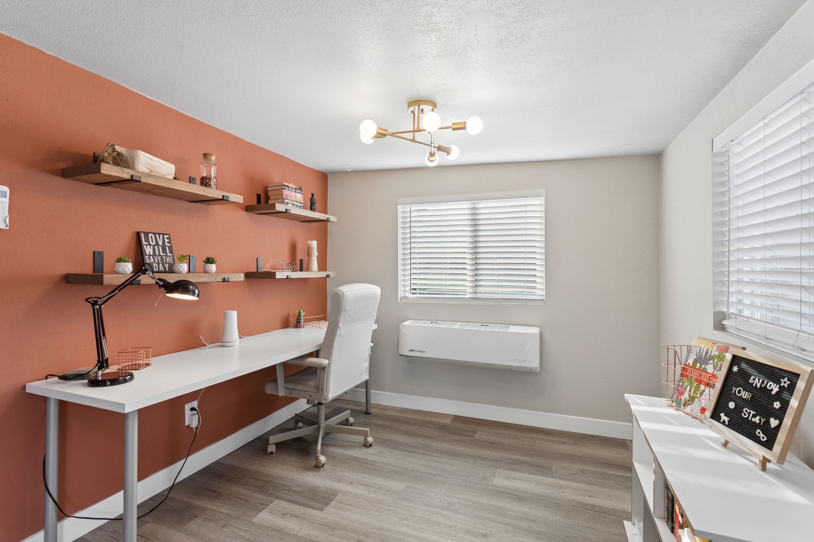 Your dedicated workspace features a warm coral accent wall, floating shelves, and modern lighting—perfect for productive remote work sessions.