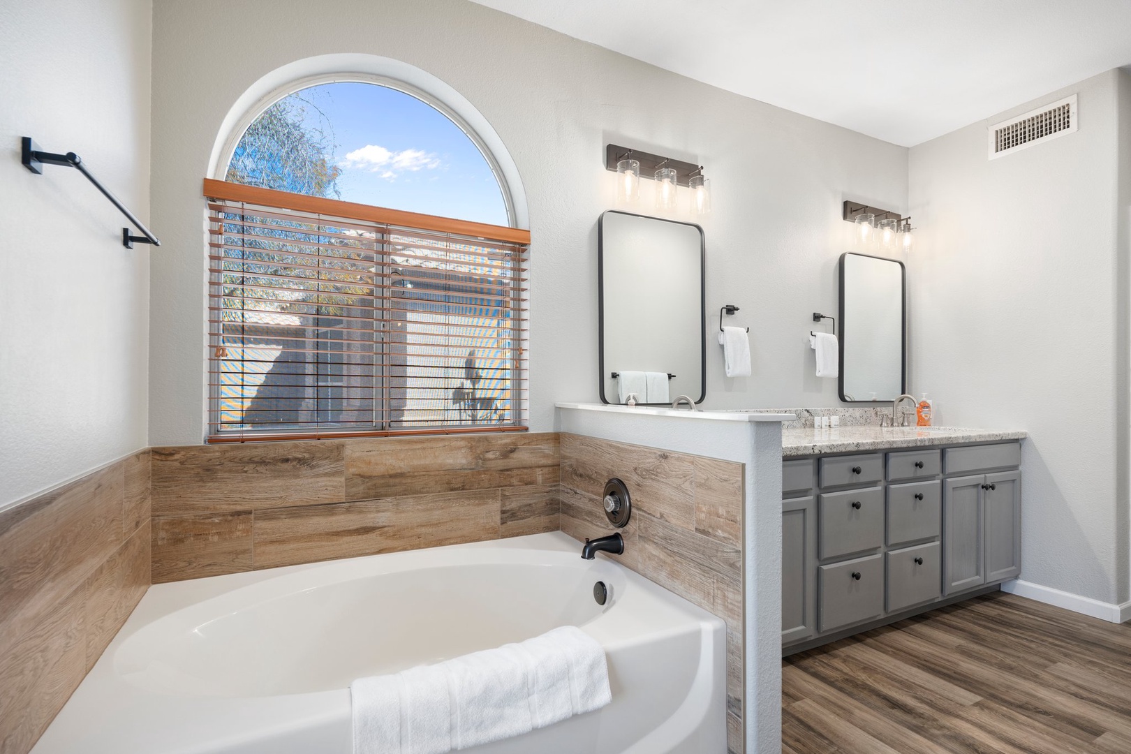 Primary suite bathroom includes a soaking tub beneath natural light from the arched window, or refresh at the spacious dual vanity with granite countertops and ample storage.