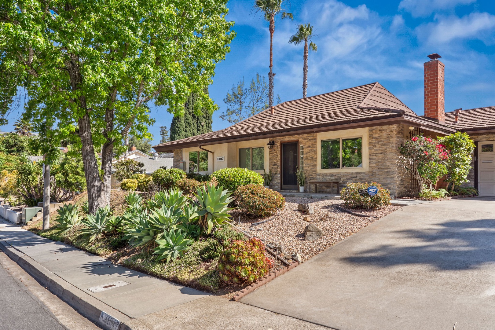 Charming stone-clad home with drought-resistant landscaping and mature palm trees in a peaceful residential neighborhood.