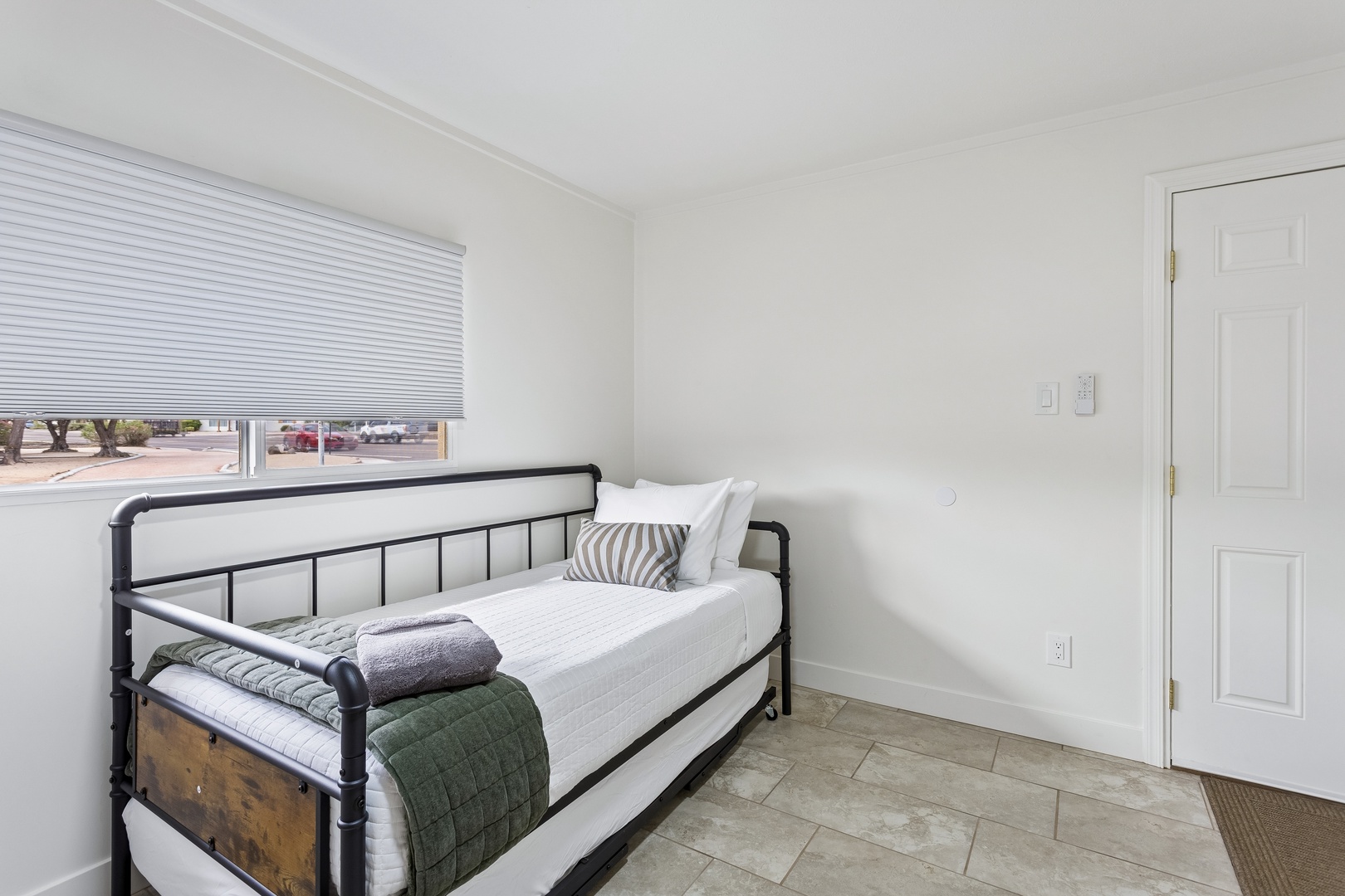 Settle into your bright, minimalist sleeping space with crisp white linens and soft natural light filtering through the window blinds.