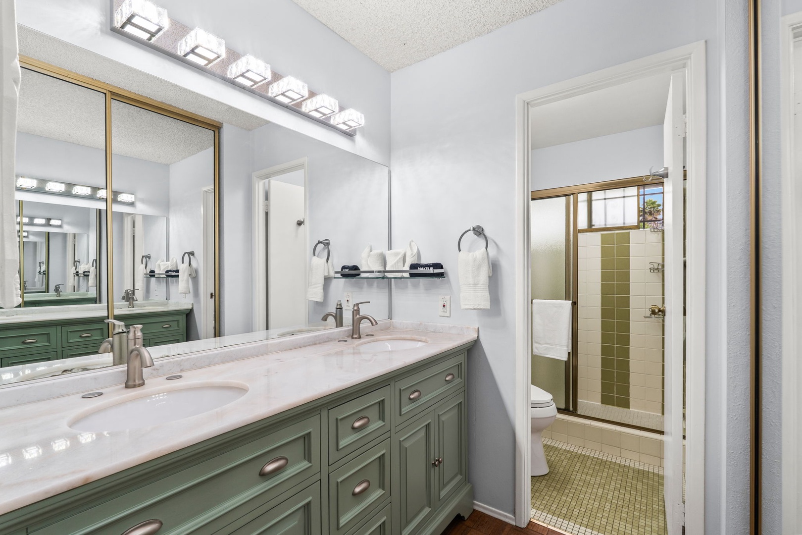 Refresh in your elegant dual-vanity bathroom featuring marble counters and sage cabinetry, with pristine towels and toiletries ready for your stay.