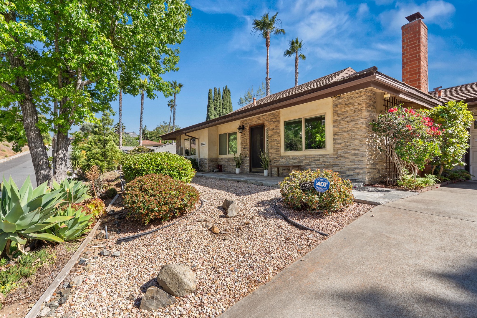 A beautifully landscaped property nestled among mature trees and drought-resistant plants in a peaceful residential setting.