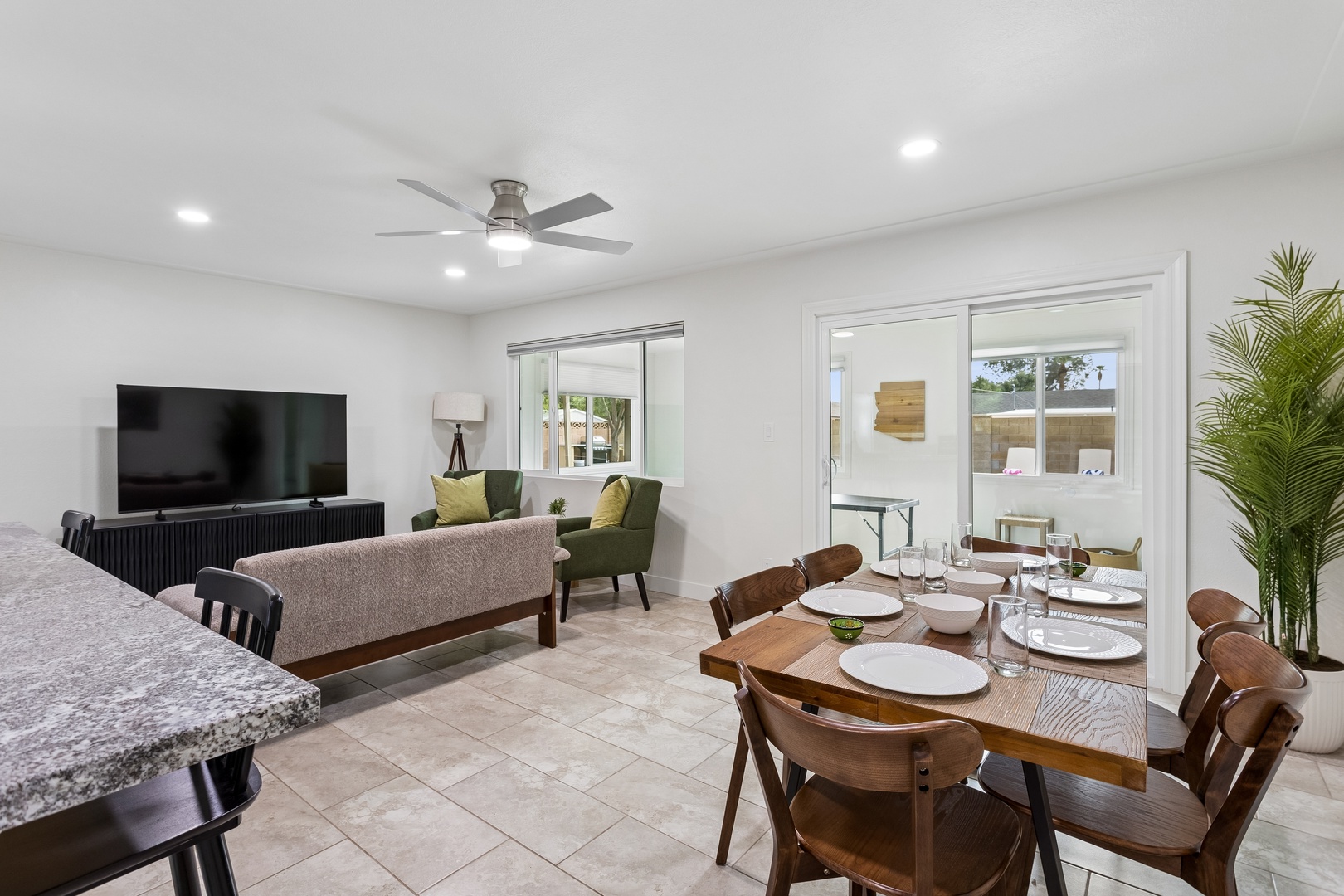 Your open-concept living and dining space invites relaxation with a cozy seating area, elegant dining table for eight, and palm trees that add a tropical touch.