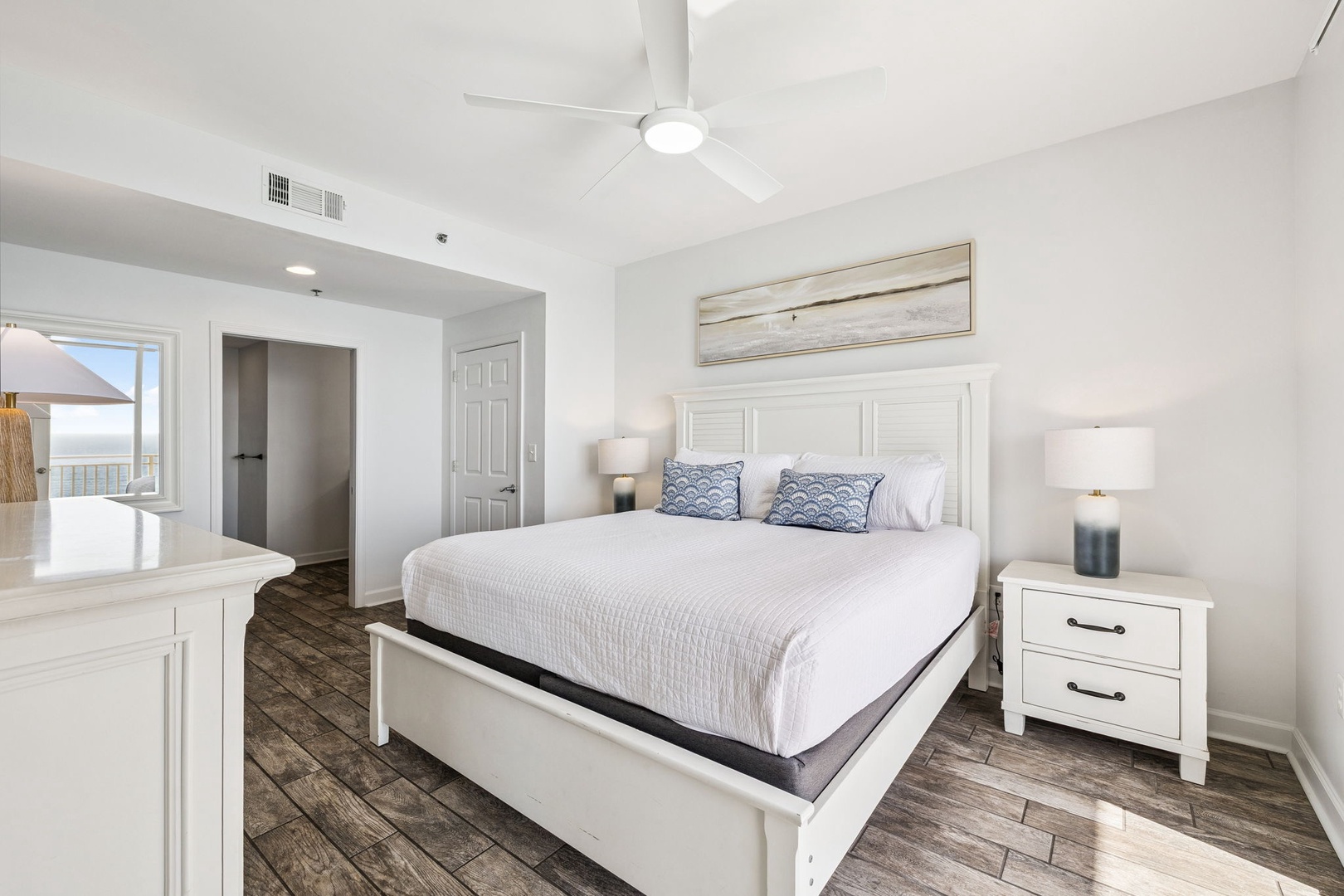 Sink into your crisp white linens and blue accent pillows in this bright, coastal bedroom with ceiling fan and tranquil views.