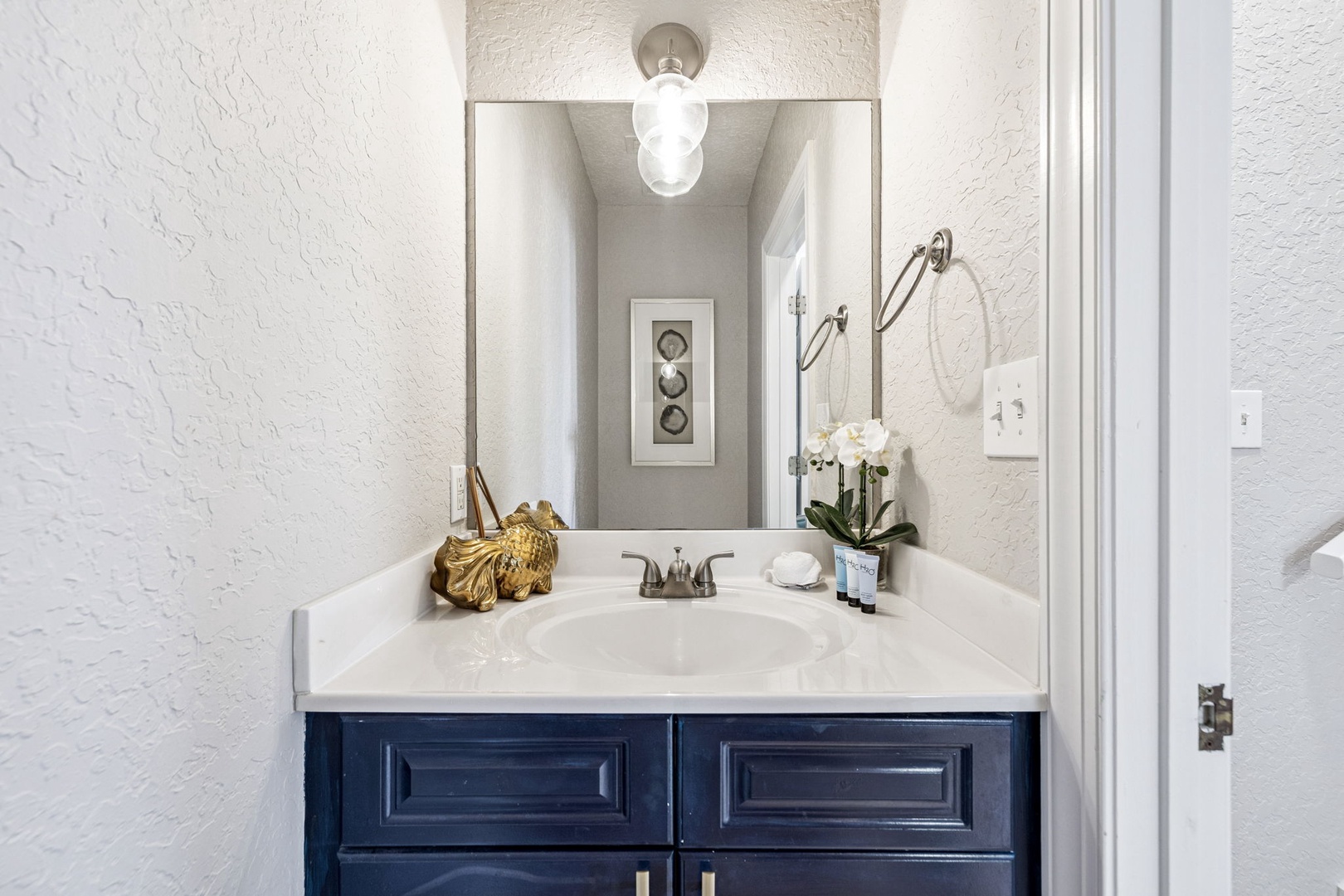 Step into your elegantly appointed powder room featuring marble countertops, thoughtful lighting, and fresh orchids welcoming you home.