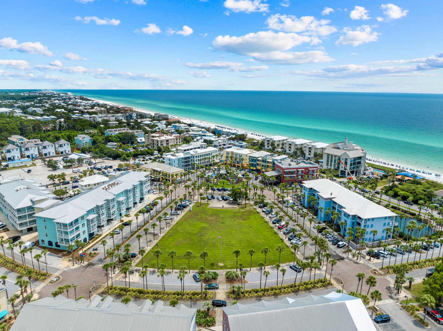 Aerial view of a vibrant coastal community featuring modern beachfront buildings and pristine white sand beaches along crystal-clear turquoise waters.