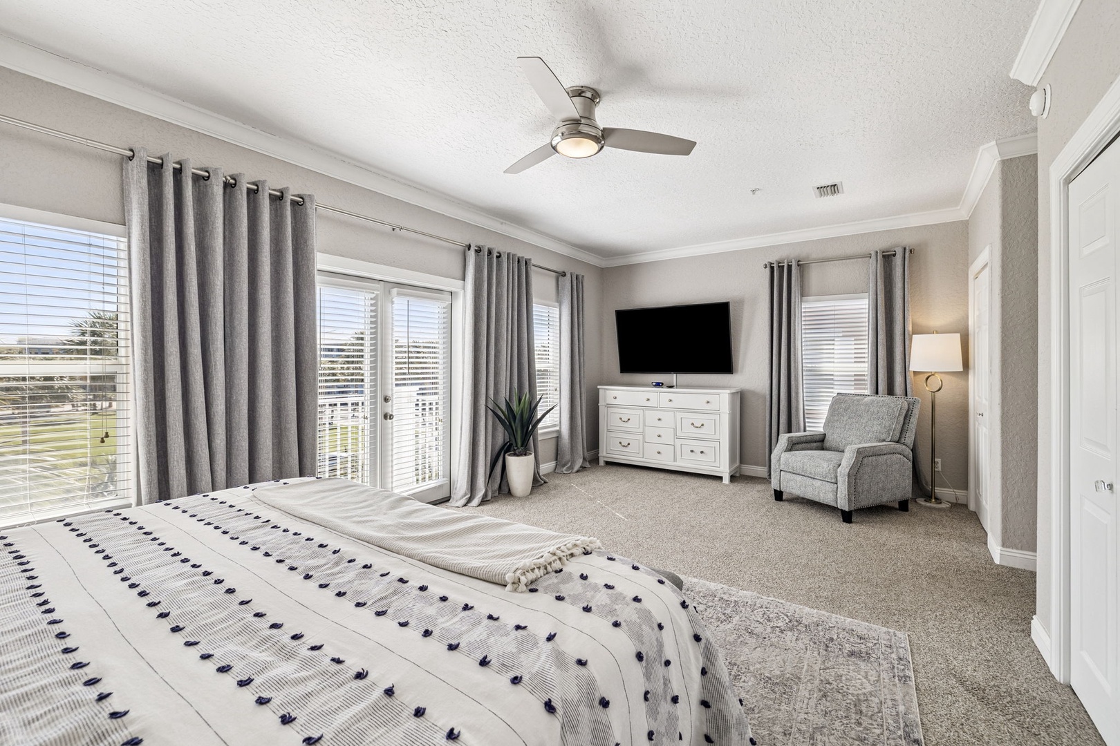 Unwind in your spacious master bedroom with plush carpeting, cozy reading chair, and natural light streaming through elegant windows.
