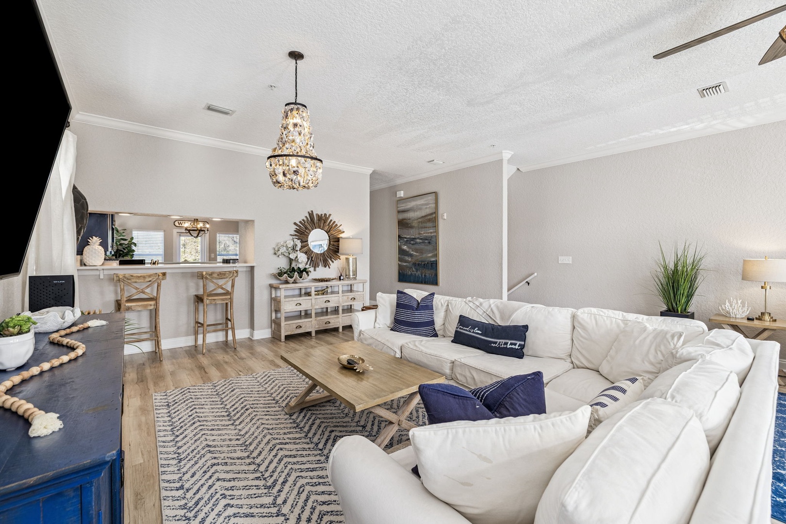 Sink into this elegant living space where crystal chandeliers cast warm light over plush white sectionals and coastal-inspired décor.