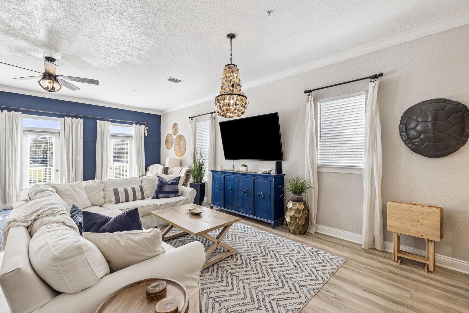 Sink into plush sofas beneath a stunning chandelier in your elegant living space, complete with entertainment center and coastal charm.