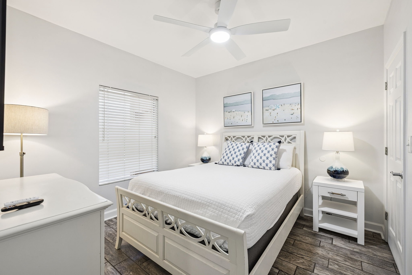 Drift off to sleep in your coastal-inspired bedroom featuring a plush white bed, soothing artwork, and gentle ceiling fan breeze.