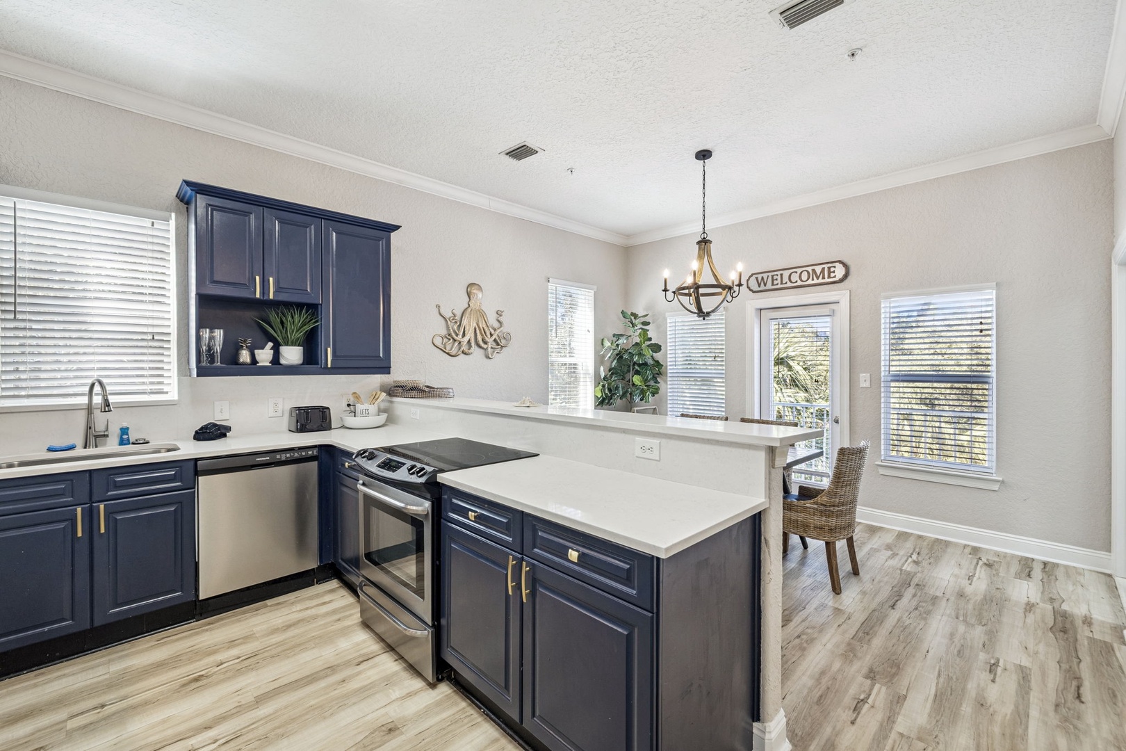 Step into your fully equipped kitchen with navy cabinets and white quartz countertops, perfect for preparing meals while enjoying natural light from multiple windows.