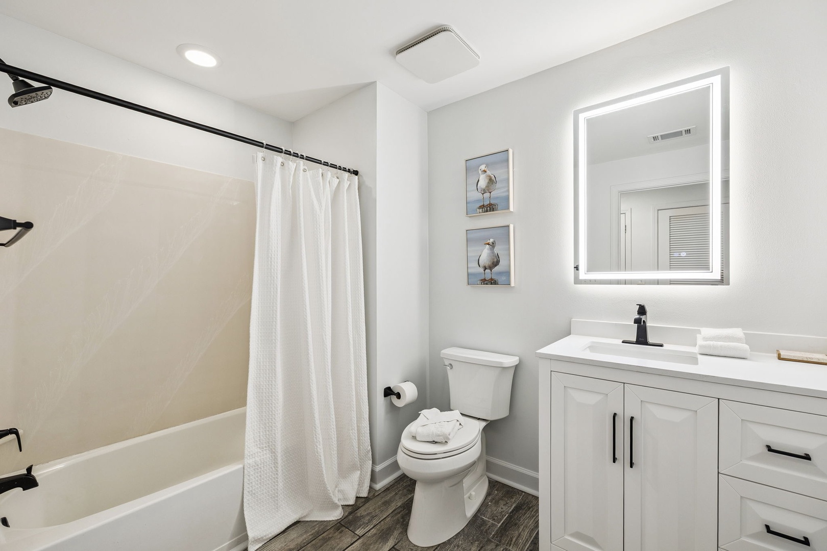 Fresh white bathroom with LED mirror lighting and coastal artwork creates your perfect morning routine space.