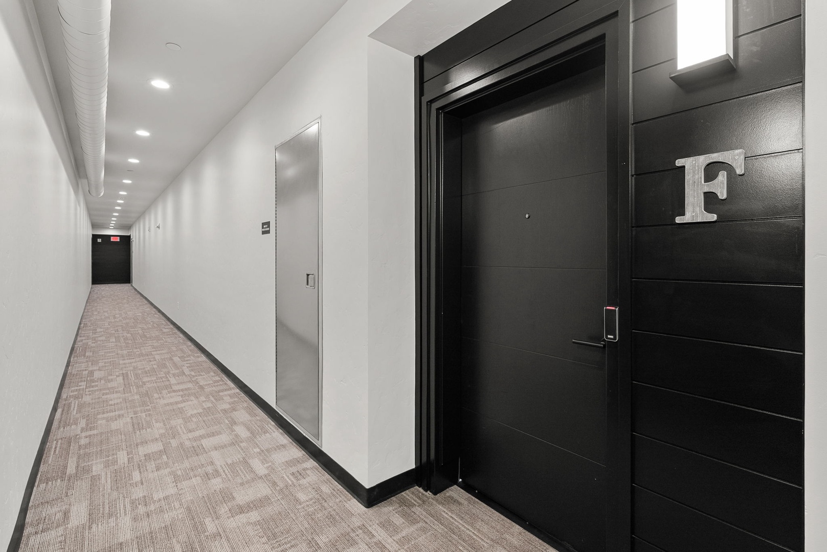 A bright, modern hallway leads to your private entrance, marked by a sleek black door with contemporary styling that sets the tone for your stay.