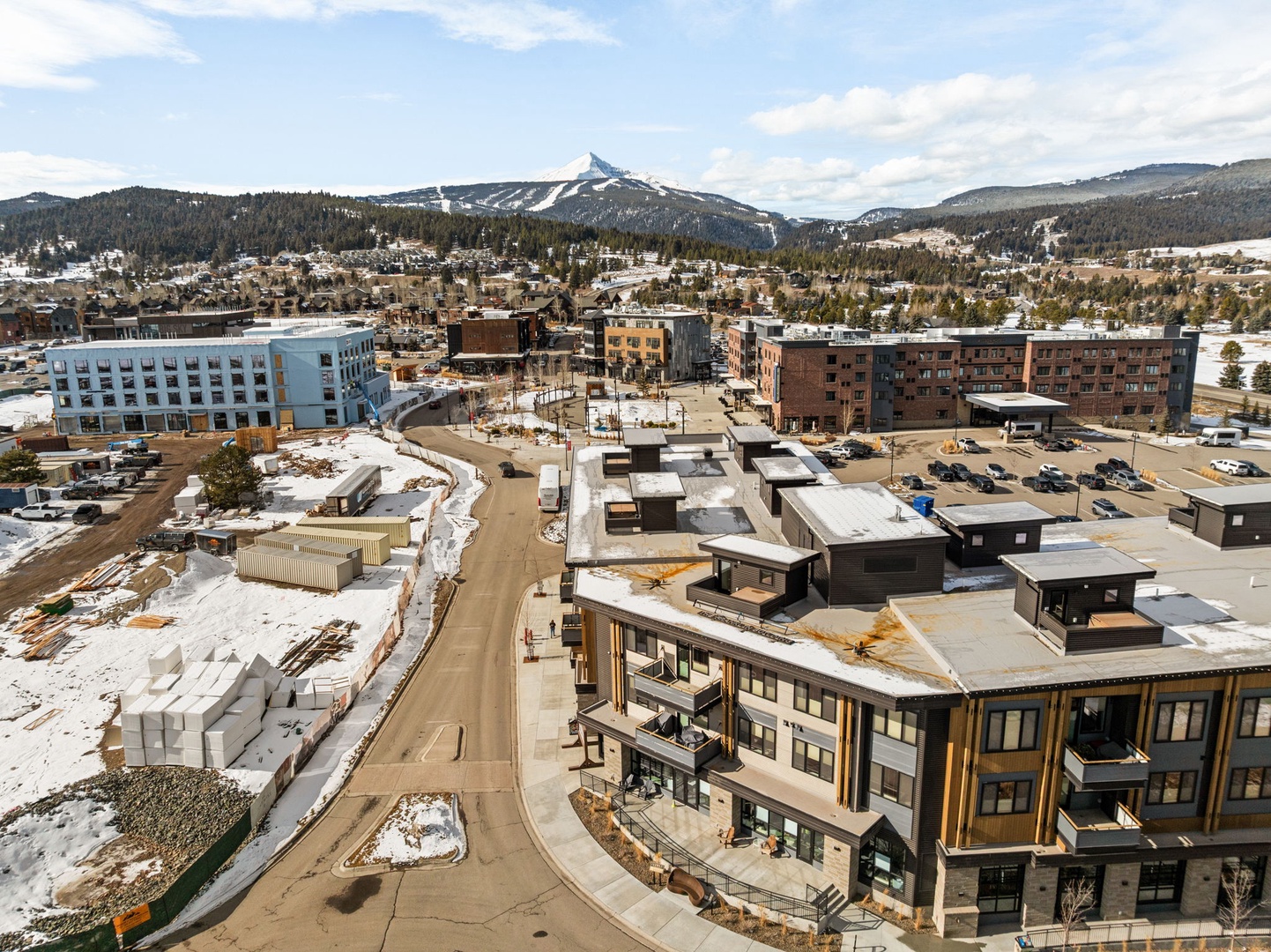 Aerial view of a developing mountain community with ski slopes visible in the distance and modern buildings nestled among forested hills.
