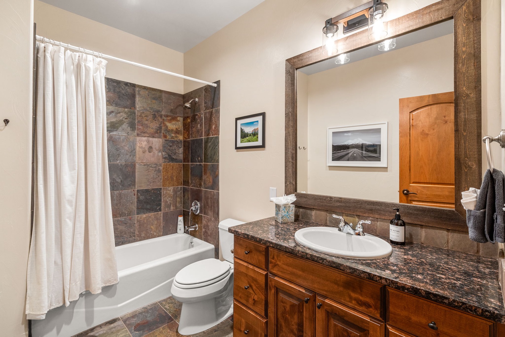 Unwind in your elegant bathroom featuring rich granite counters, slate tile shower, and warm wood vanity.