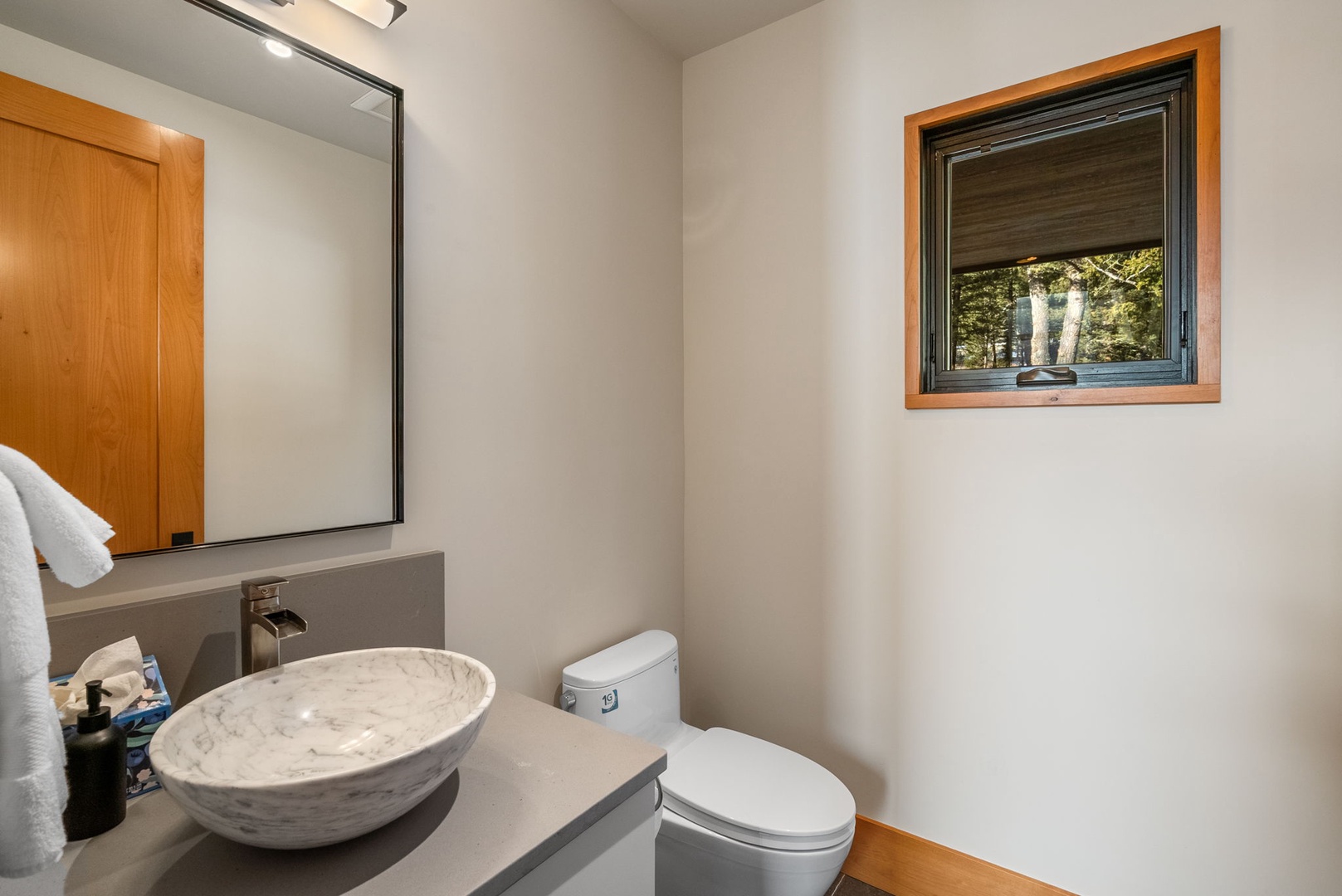 Refresh in your modern guest bathroom featuring a stunning marble vessel sink and forest views through the window.