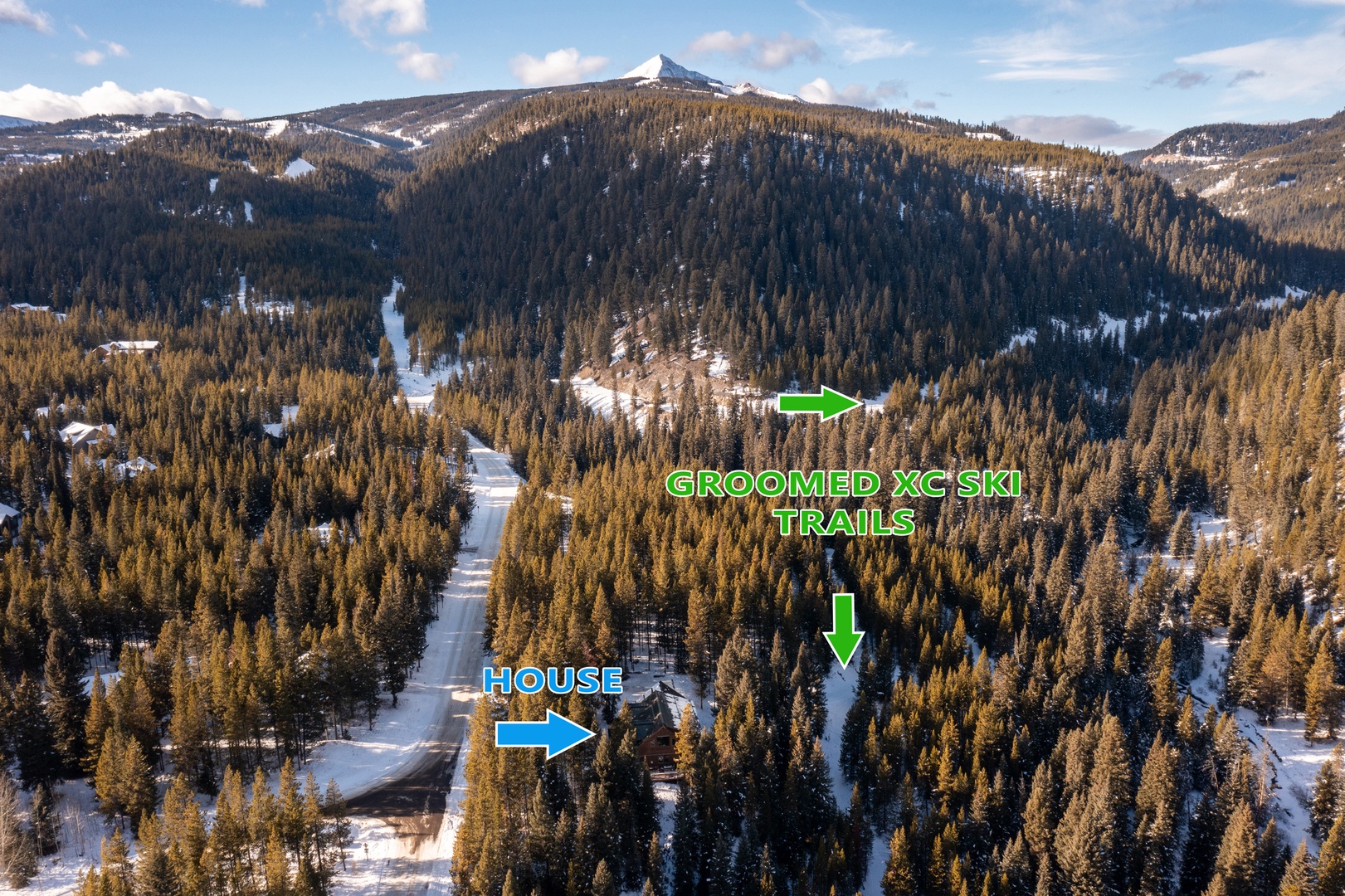 Aerial view of a mountain property nestled among snow-covered forests with groomed ski trails nearby, offering direct access to winter recreation.