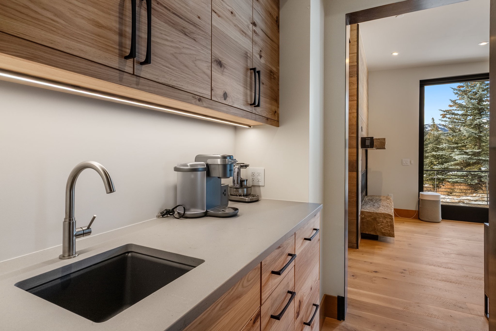 Your sleek kitchen features warm wood cabinetry, premium appliances, and stunning mountain views through the bedroom window.
