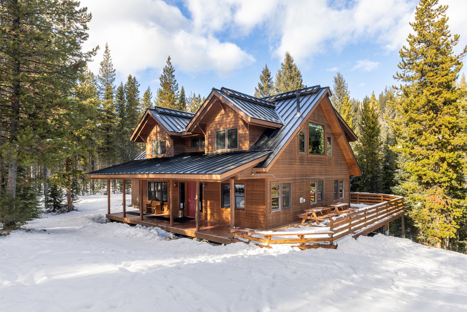 A stunning mountain cabin nestled among snow-covered pines, featuring warm wood siding and a welcoming covered porch.