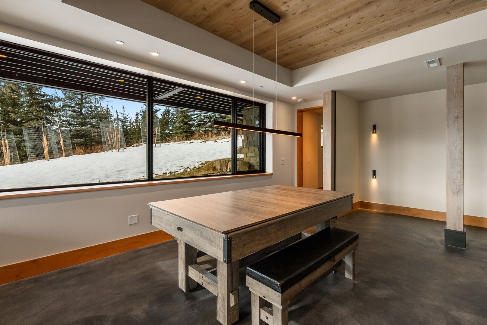 Gather around this rustic dining table with stunning winter mountain views through floor-to-ceiling windows in your modern mountain retreat.