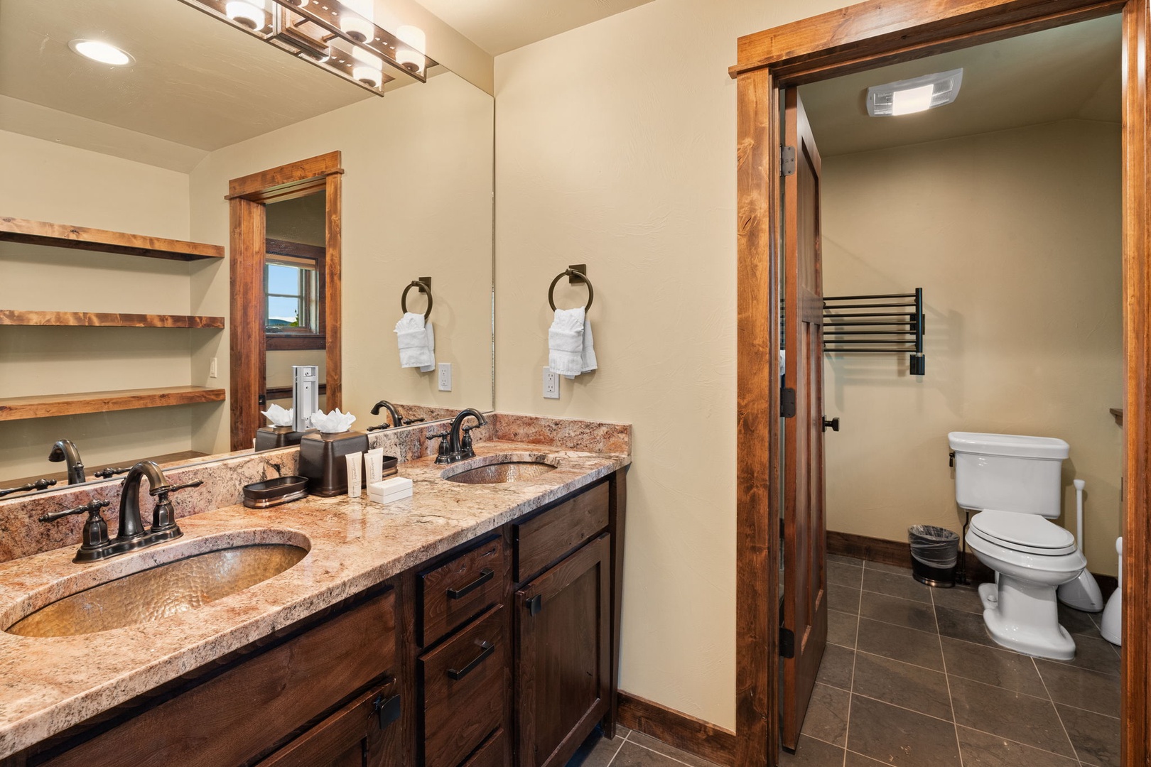 Refresh in your private en-suite bath featuring dual vanities, rustic wood accents, and thoughtful touches like plush towels and a separate water closet for added convenience.