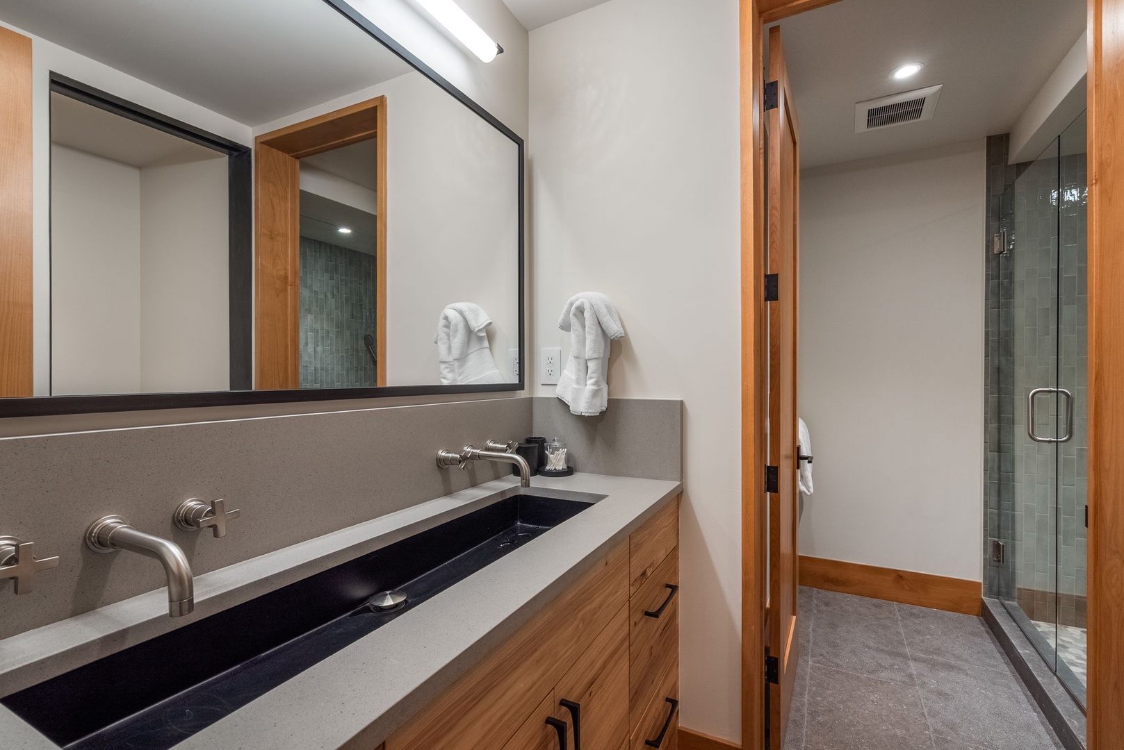 Step into your spa-inspired bathroom featuring a stunning dual vanity with sleek stone counters, warm wood accents, and a spacious glass shower.