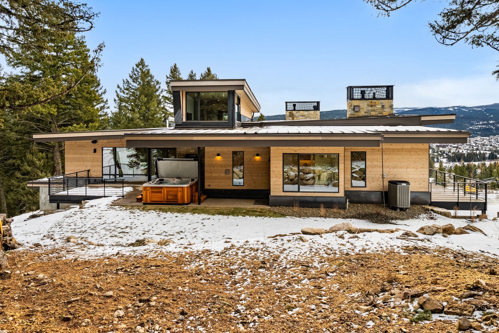 Modern mountain retreat featuring contemporary architecture surrounded by snowy landscape and towering evergreens with scenic valley views.