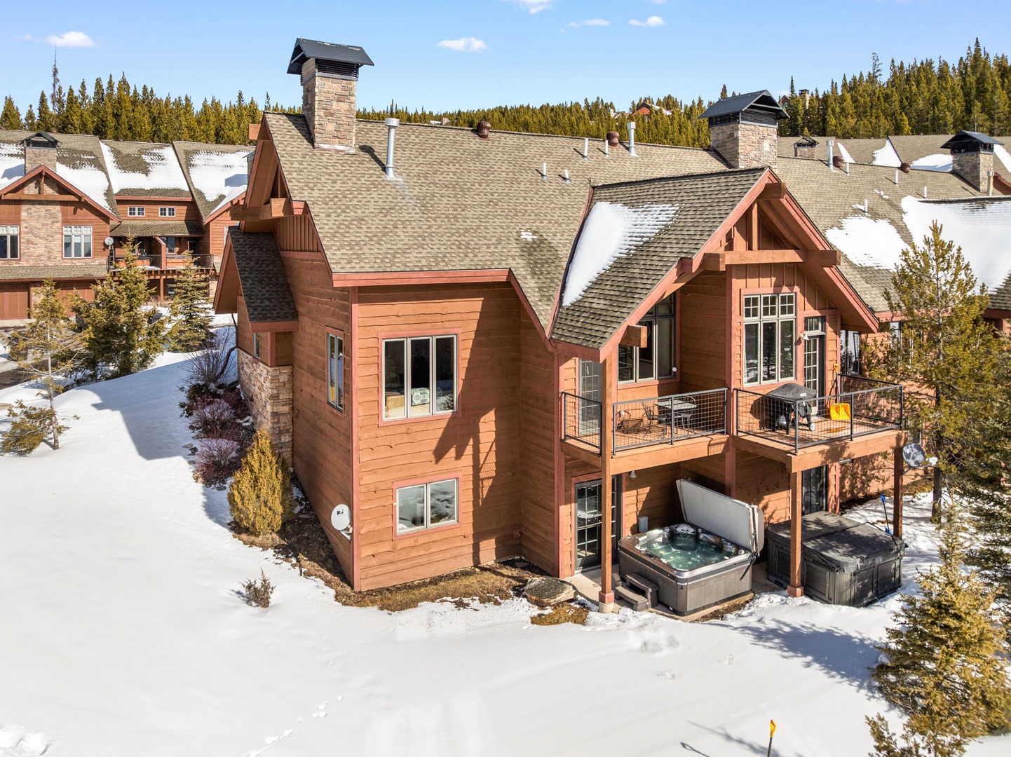 Mountain chalet features rustic wood siding and private hot tub surrounded by pristine winter landscape and evergreen forest backdrop.